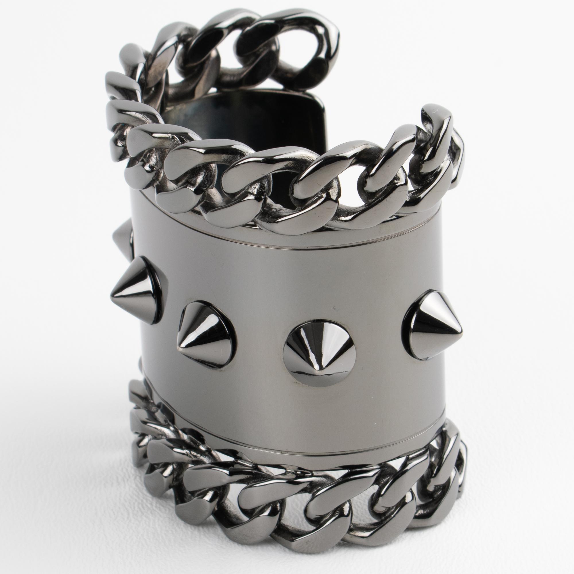 Make a bold statement with this exceptional Givenchy Paris bangle bracelet, a rare and striking example of brutalist design. Crafted in high-gloss gunmetal, the oversized cuff showcases dramatic contours and is adorned with edgy chain and stud