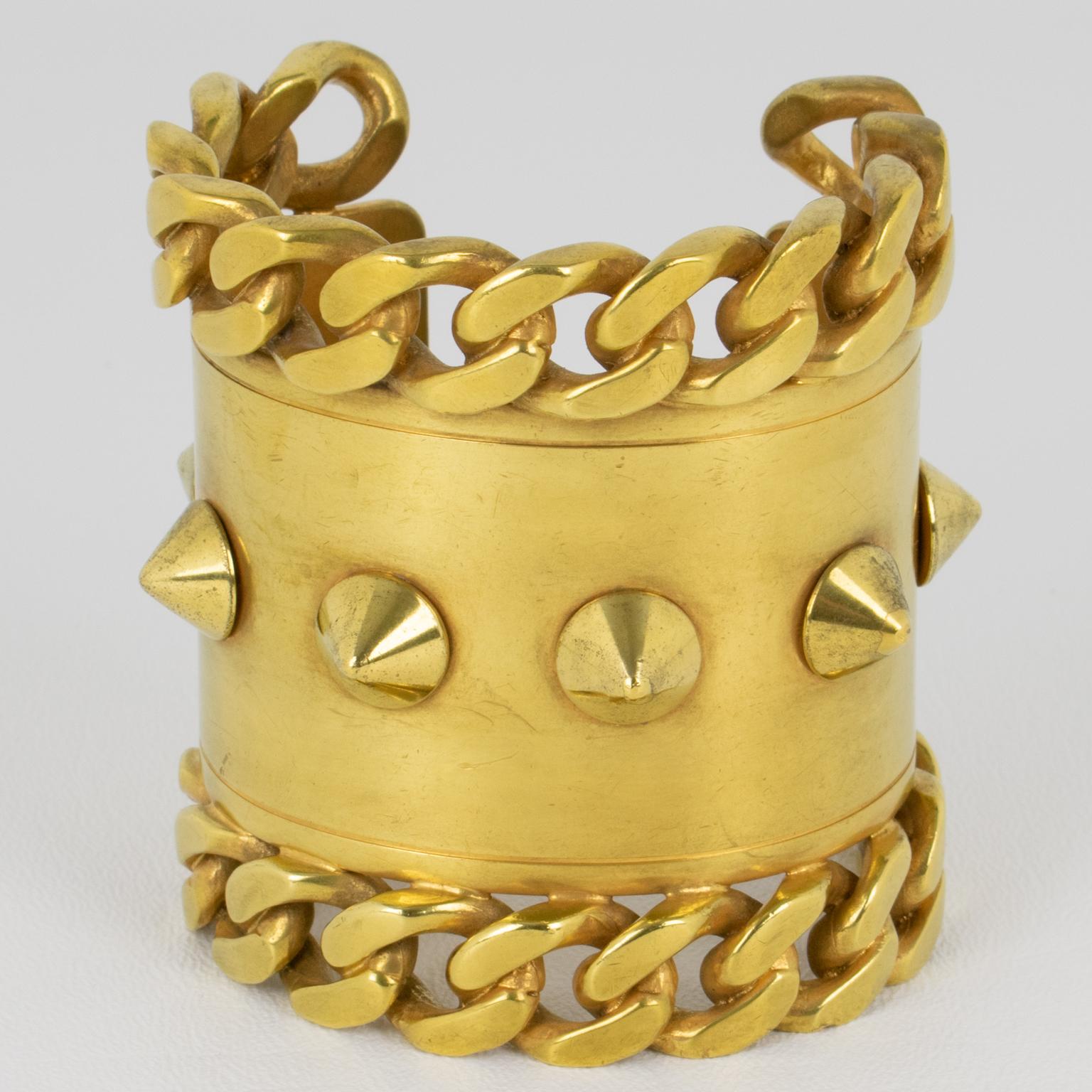 Ce superbe bracelet-bracelet Givenchy Paris arbore une forme massive de manchette brutaliste. Cette pièce rare est fabriquée en laiton doré et ornée de chaînes et de clous. L'intérieur du bracelet manchette est gravé Givenchy. 
Dimensions : La