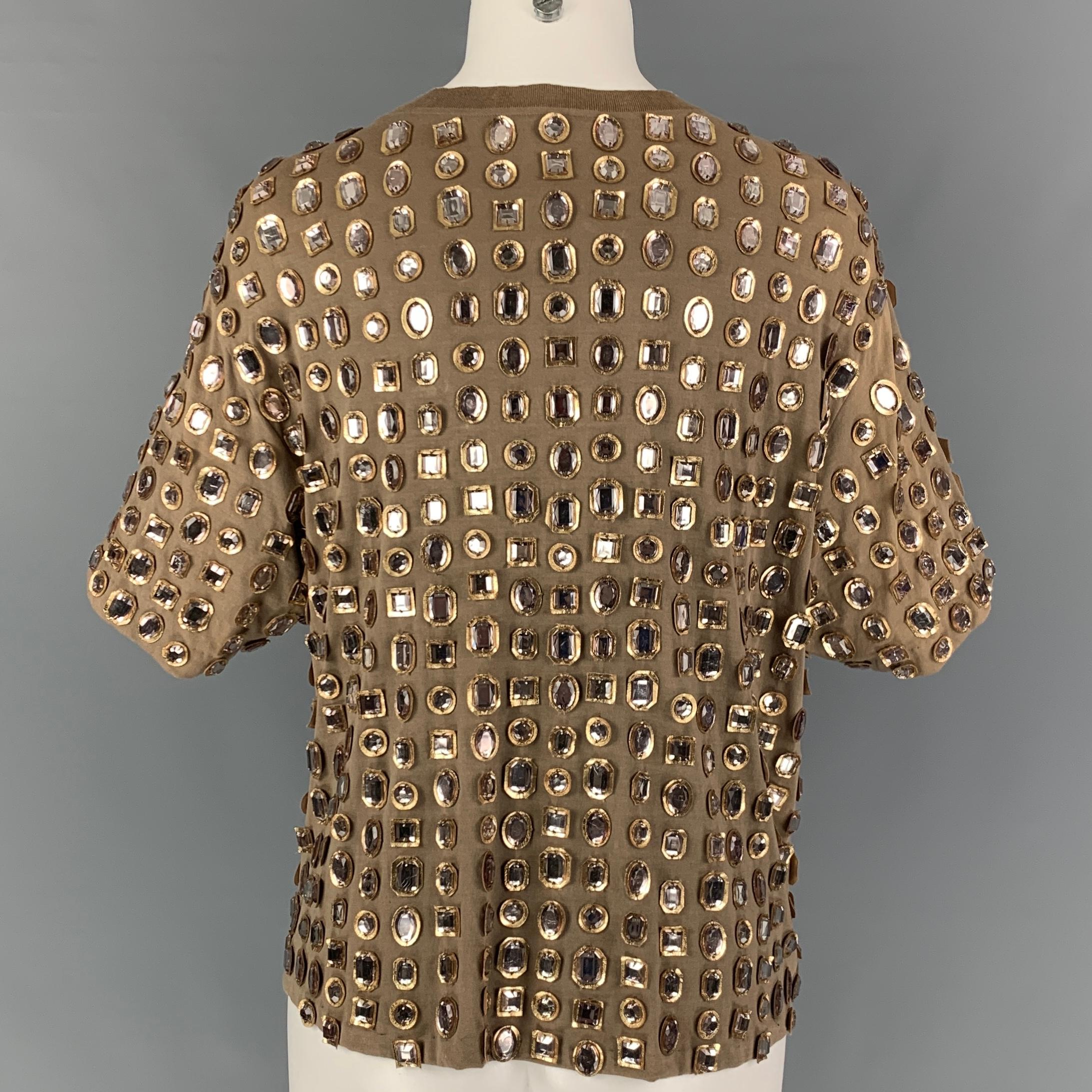 GIVENCHY top comes in a taupe material featuring gold leather details, rhinestone embellishments, and a crew-neck.

Very Good Pre-Owned Condition. Fabric tag removed.
Marked: M

Measurements:

Shoulder: 19 in.
Bust: 40 in.
Sleeve: 9.5 in.
Length: 21