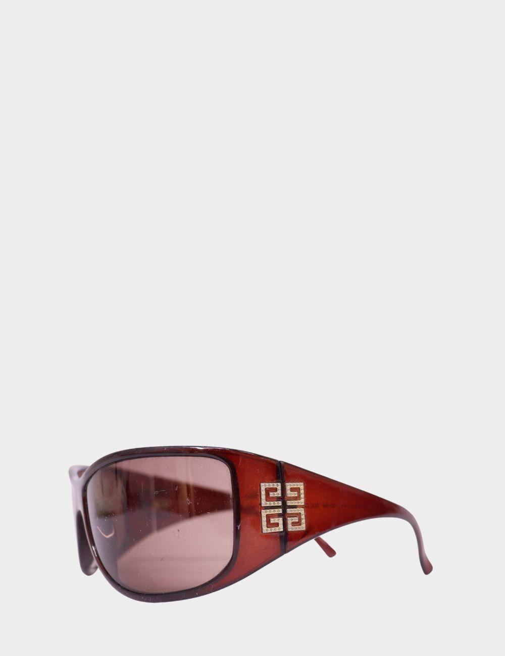 Eleva il tuo look con questi occhiali da sole avvolgenti vintage di Givenchy. Caratterizzati da un'audace montatura in acetato bordeaux e da aste larghe ornate dall'iconico logo Givenchy a doppia G con dettagli dorati, questi occhiali da sole