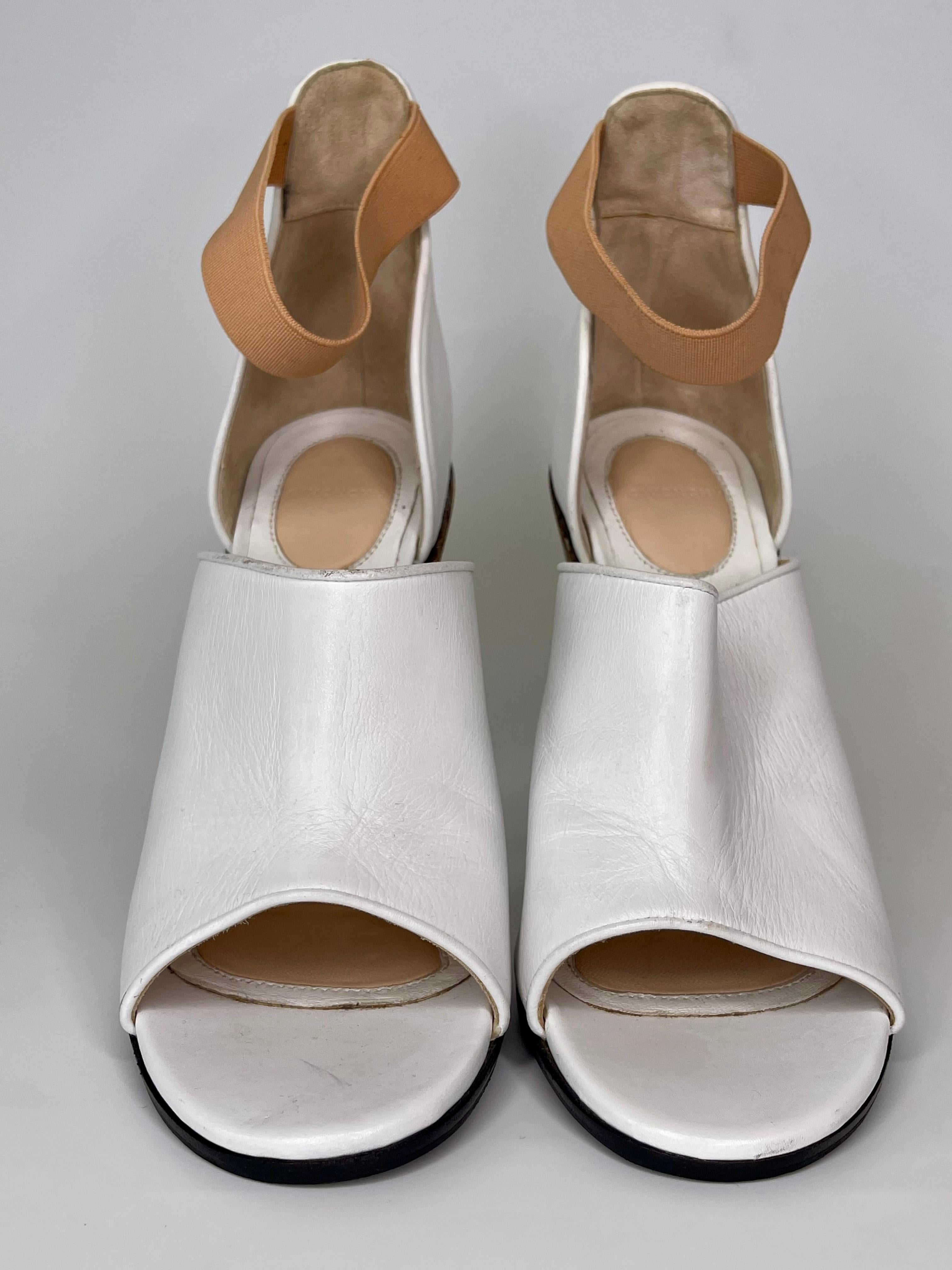 From the 2013 Collection, this Givenchy Open Toe Heel features a wooden conical heel with gold finishing and a white leather upper studded at the bottom. The shoe is held in place on the foot by a blush color strap. 

COLOR: White
MATERIAL: Leather
