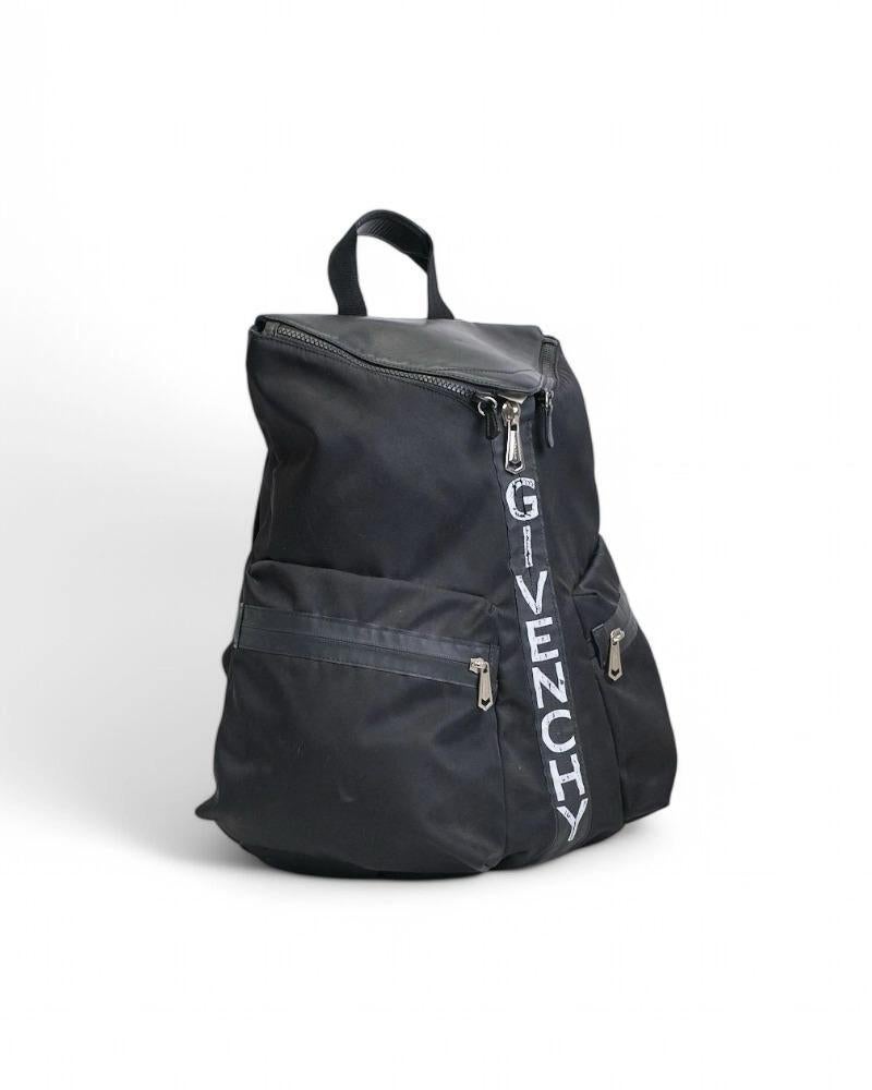 Der charakteristische Rucksack von Givenchy, Modell Triangle, aus schwarzem Nylon mit Lederbesatz und Palladium-Hardware. Der Rucksack ist mit einem asymmetrischen Verschluss ausgestattet, innen mit Ton-in-Ton-Nylon gefüttert und sehr geräumig.