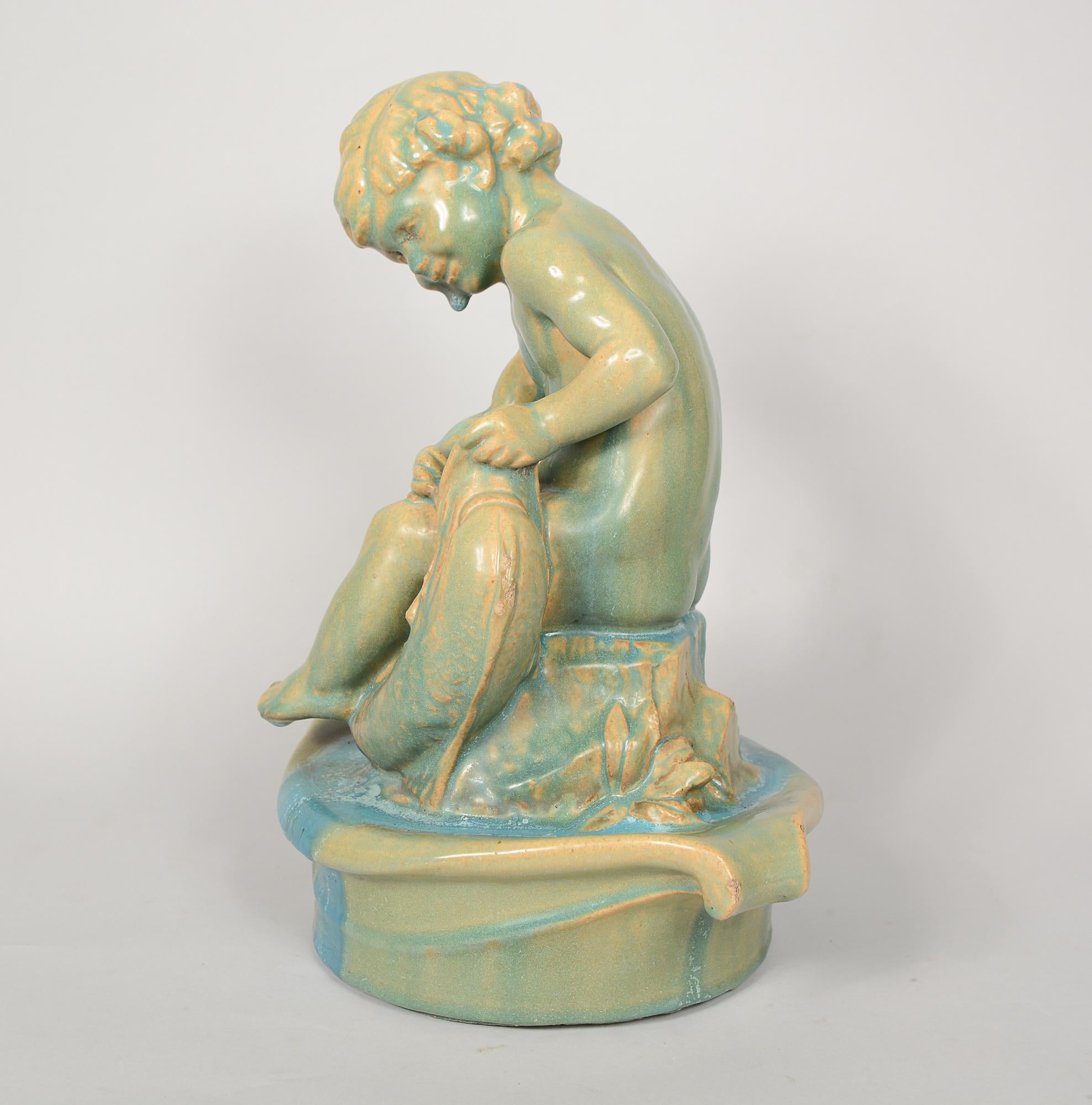 Fountain center piece of a child with a fish by the California pottery company, Gladding McBean. This has a dripping aqua blue glaze with the base clay showing through in areas. There are some chips to the piece, the hair has one, one toe, the