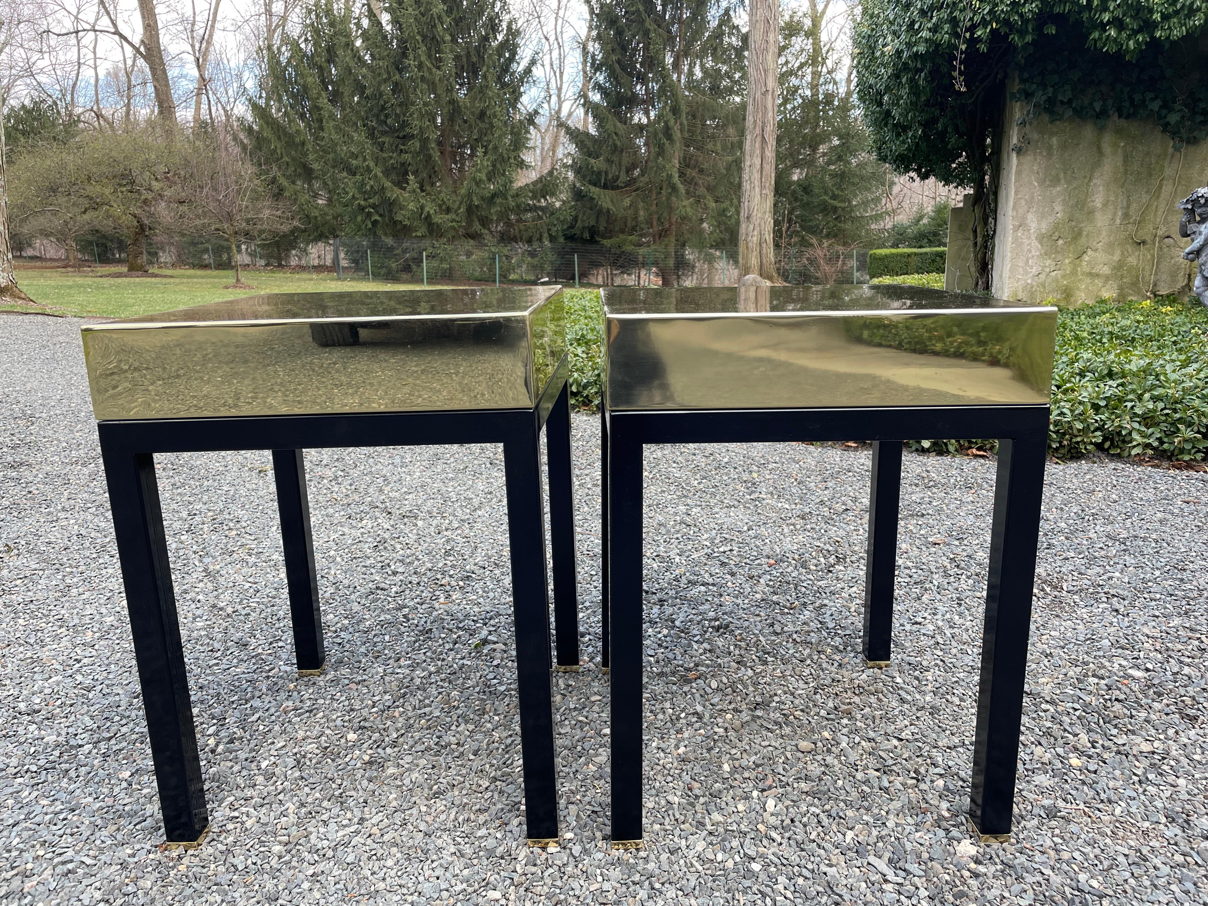 Stunning pair of sleek glistening end or side tables construsted of thick brass tops and ebonized wood bases. The brass has been polished and lacqered for protection. The feet are brass capped. There are 3/8