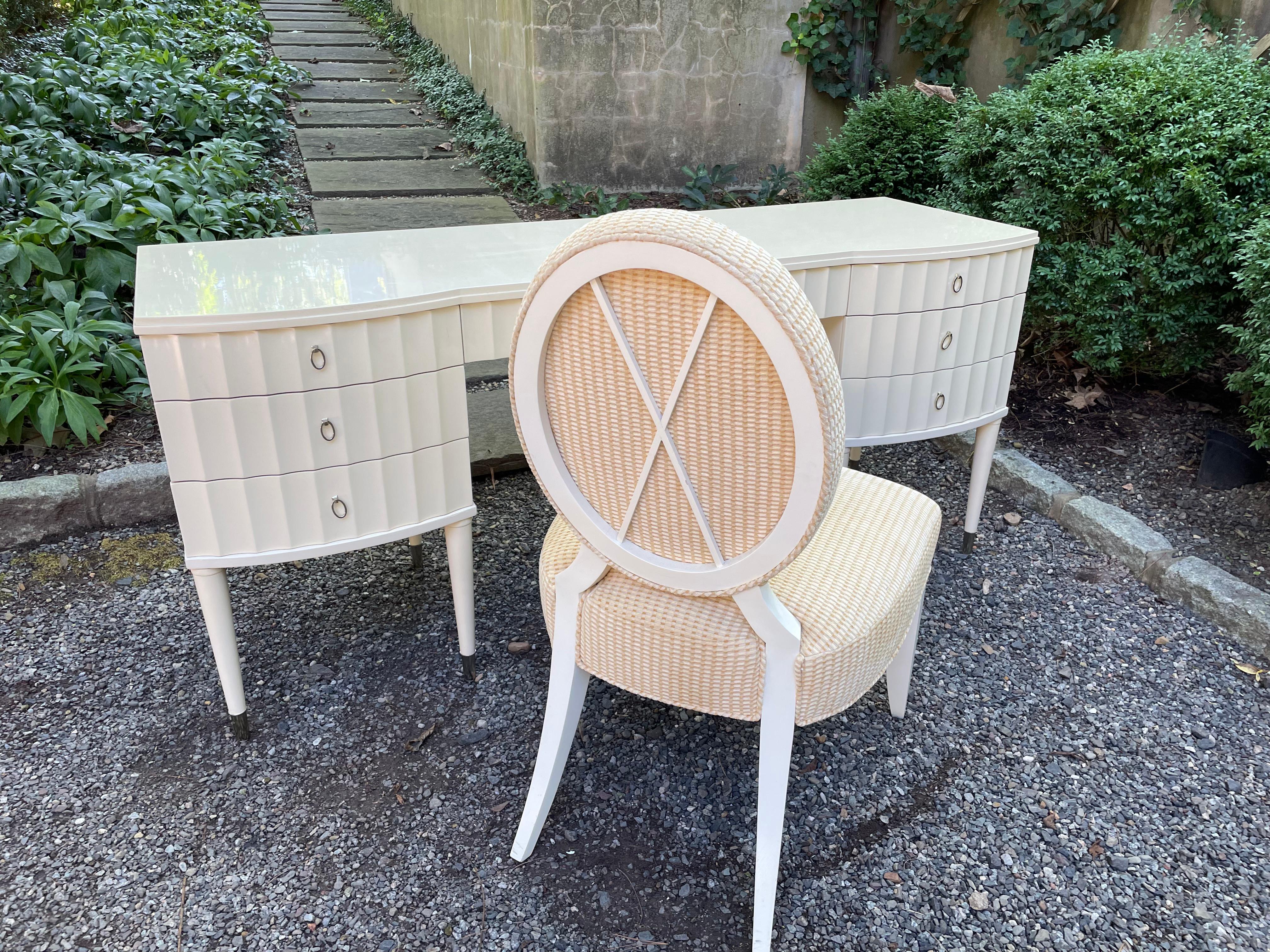 Glamorous designer desk or vanity and accompanying chair by Barbara Barry for Baker. Both are finished in a cream colored lacquer. The desk has seven fluted drawers. The feet of the desk are each cuffed in brushed nickel. Knee clearance measures