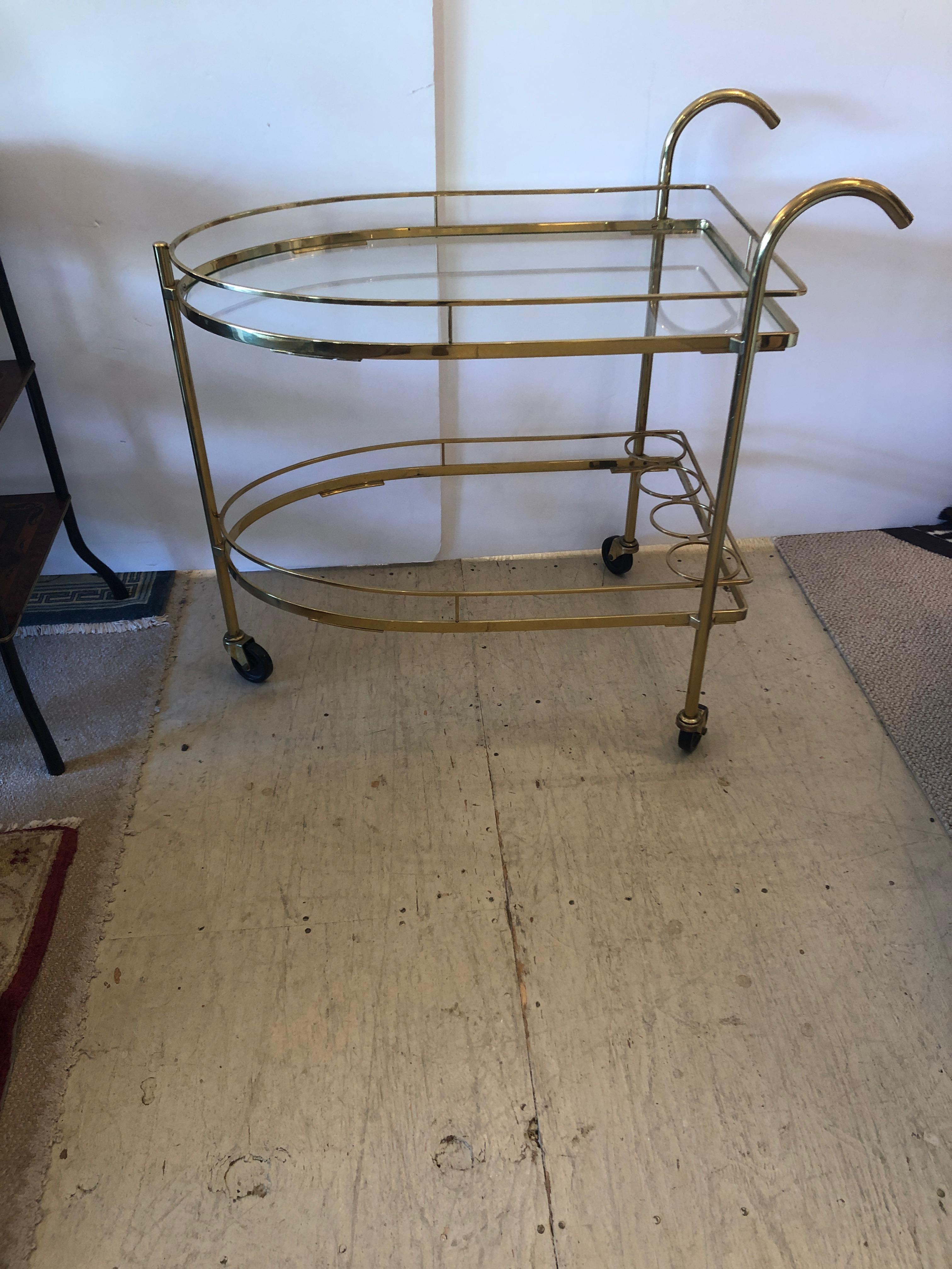 Schnazzy brass and glass bar cart in an unusual arch shape, having 2 tiers and cane like handles. Lower tier has new glass and wine or bottle rack. Height to top tier 29.