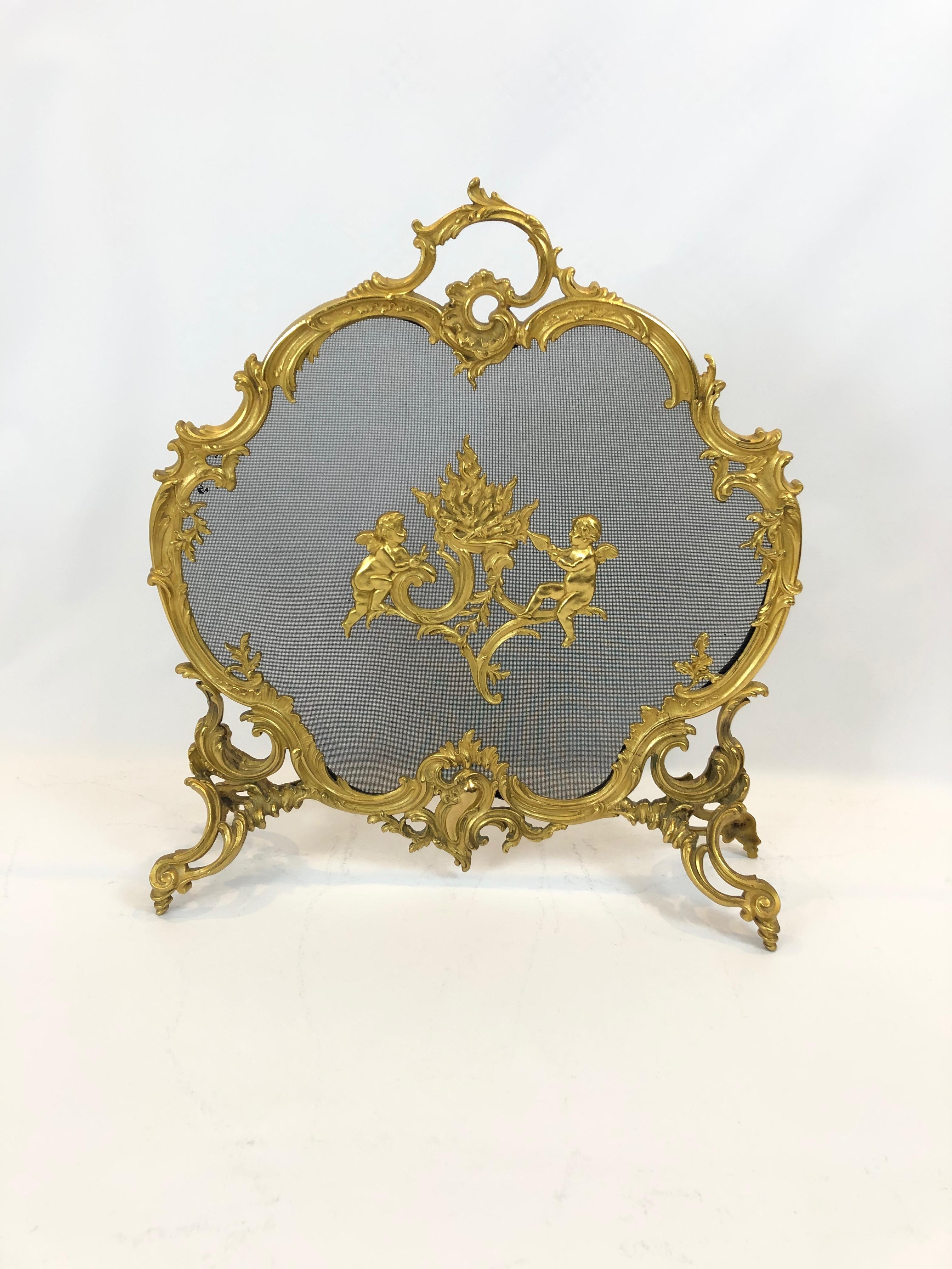 A superbly pretty sculptural fireplace screen having a scalloped rounded bronze dore frame in fancy French style, central pair of cherubs on the front of the screen and ornate feet.