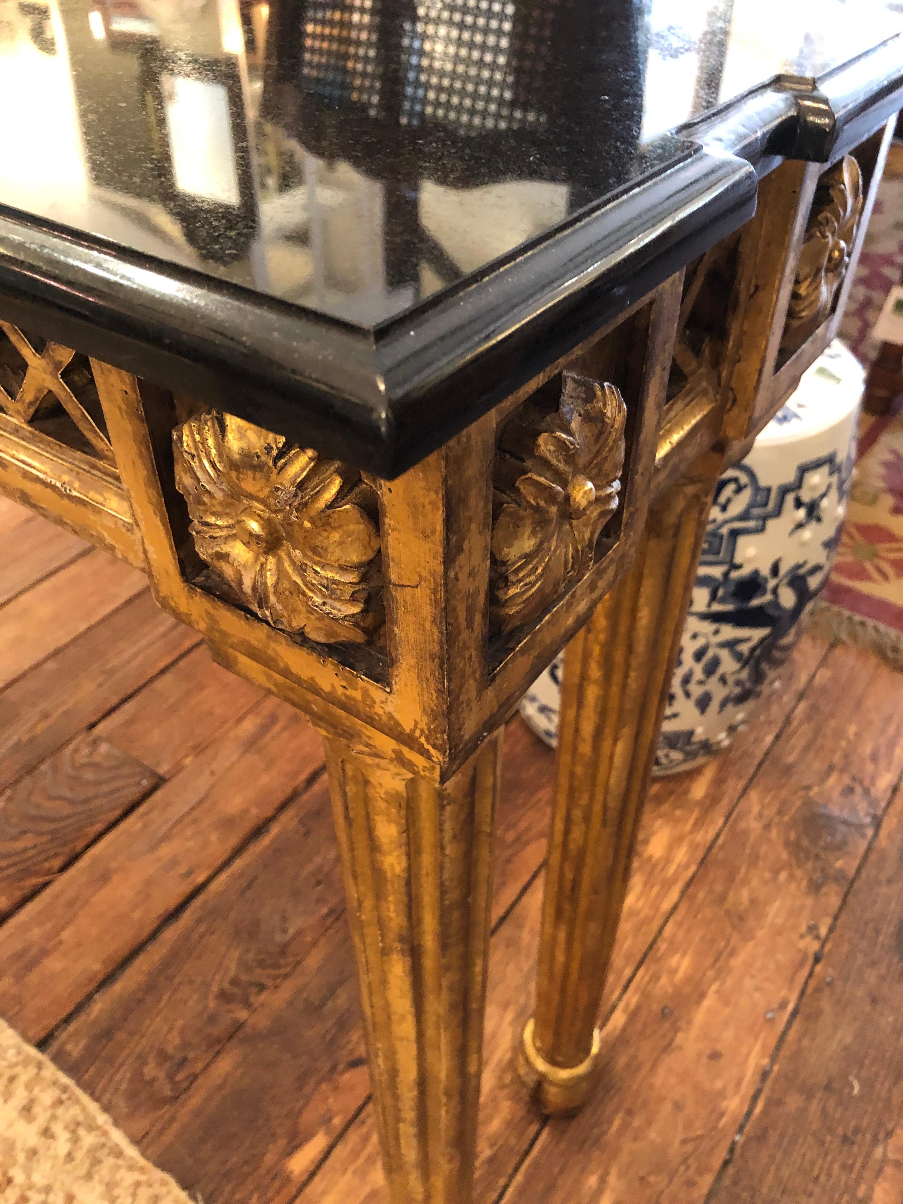 Glamorous blend of gold and black in this Hollywood Regency giltwood and marble console table. The center rams head adds a moviestar touch, and the cut out ends of the console top make the black top especially elegant. Tapered carved legs and lovely