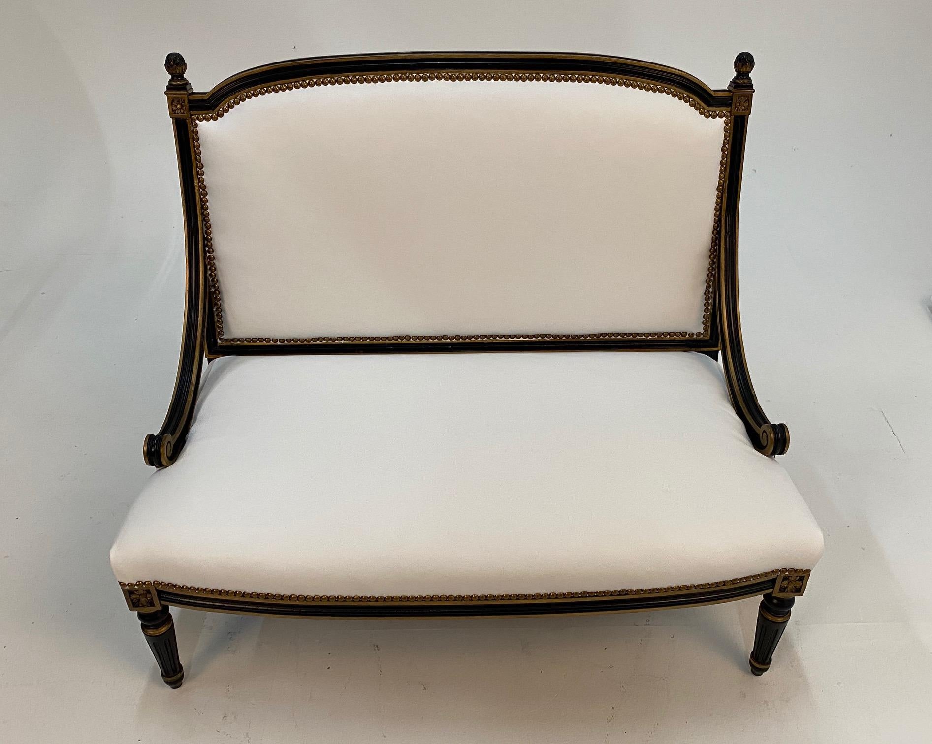 Elegant Hollywood Regency loveseat having ebonized and gilded frame with turned legs, windowpane back, low slung curved arms and brand new white leather upholstery.