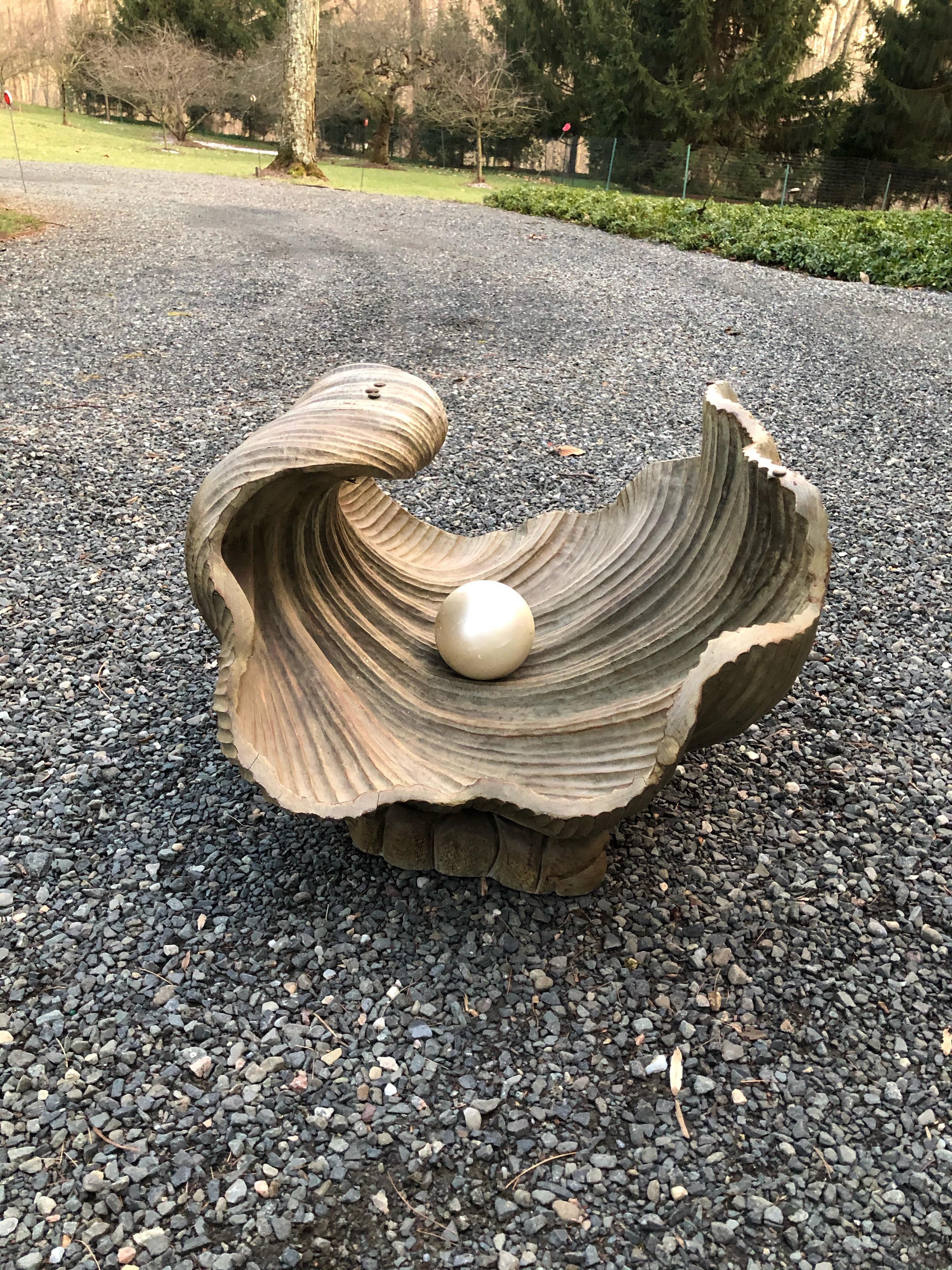 An Italian natural faux finished hand carved wood cocktail table that looks like a monumental clam shell with large pearl floating in it. The glass top is a substantial 5/8” thick with a bull nosed edge. The shell itself measures 27” wide x 21” deep