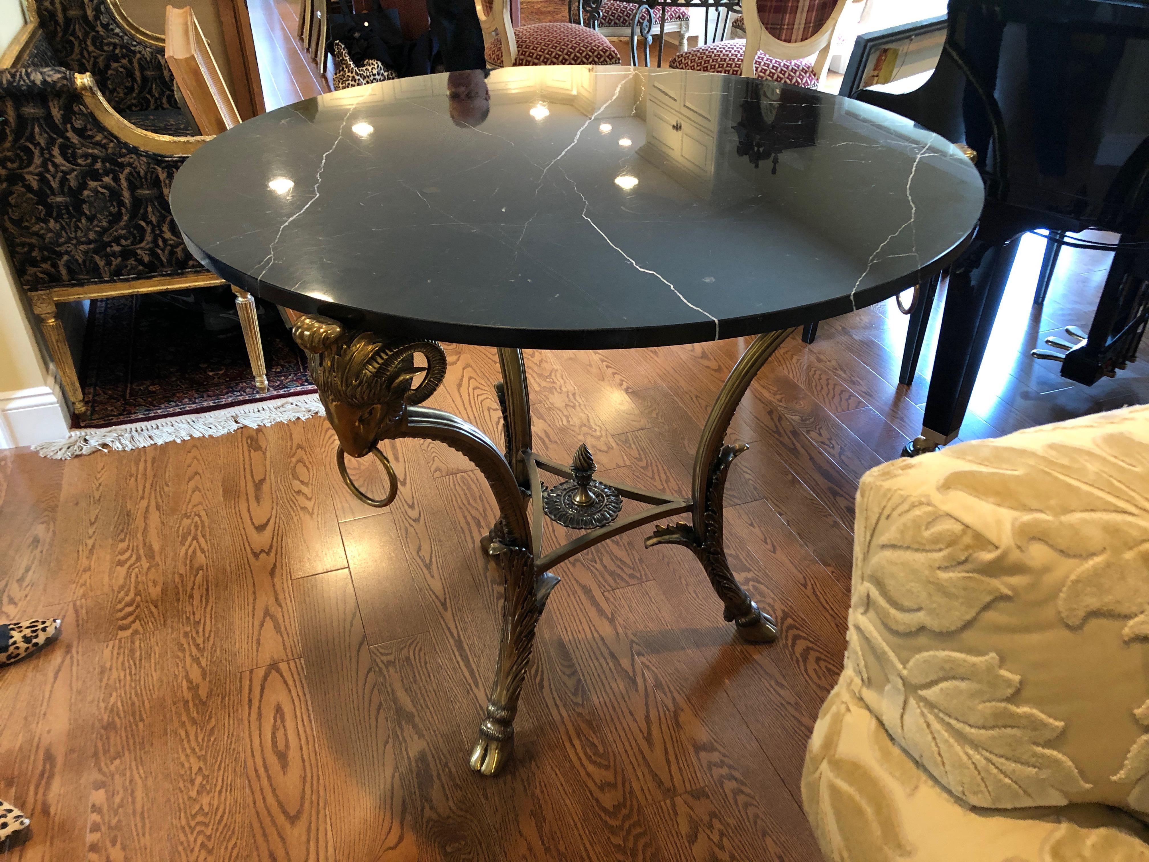 Moviestar glamorous centre round table by LaBarge, having a black marble top with white grain and sensational brass base with chunky ram's heads supporting the top, hoof feet, and a centre decorative finial.