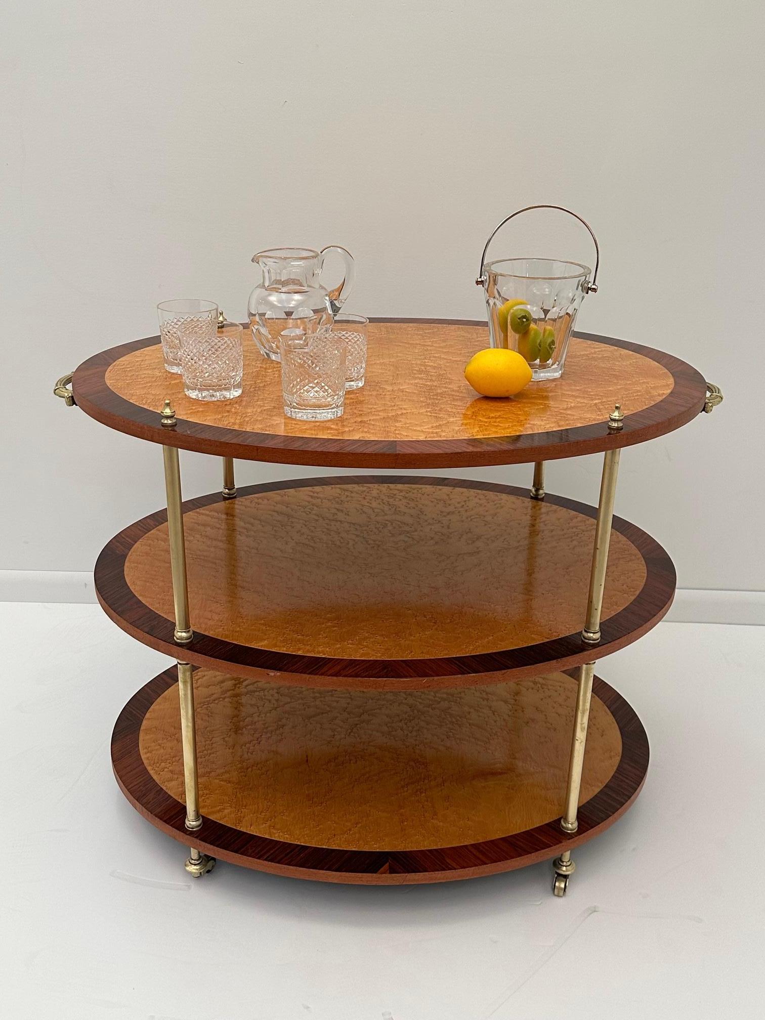 Superb vintage 3 tier serving cart having a glamorous combination of oval honey colored burl surfaces with contrasting dark mahogany inlay around the peripheries. The rods that hold the cart together are brass, as are the beautiful handles and