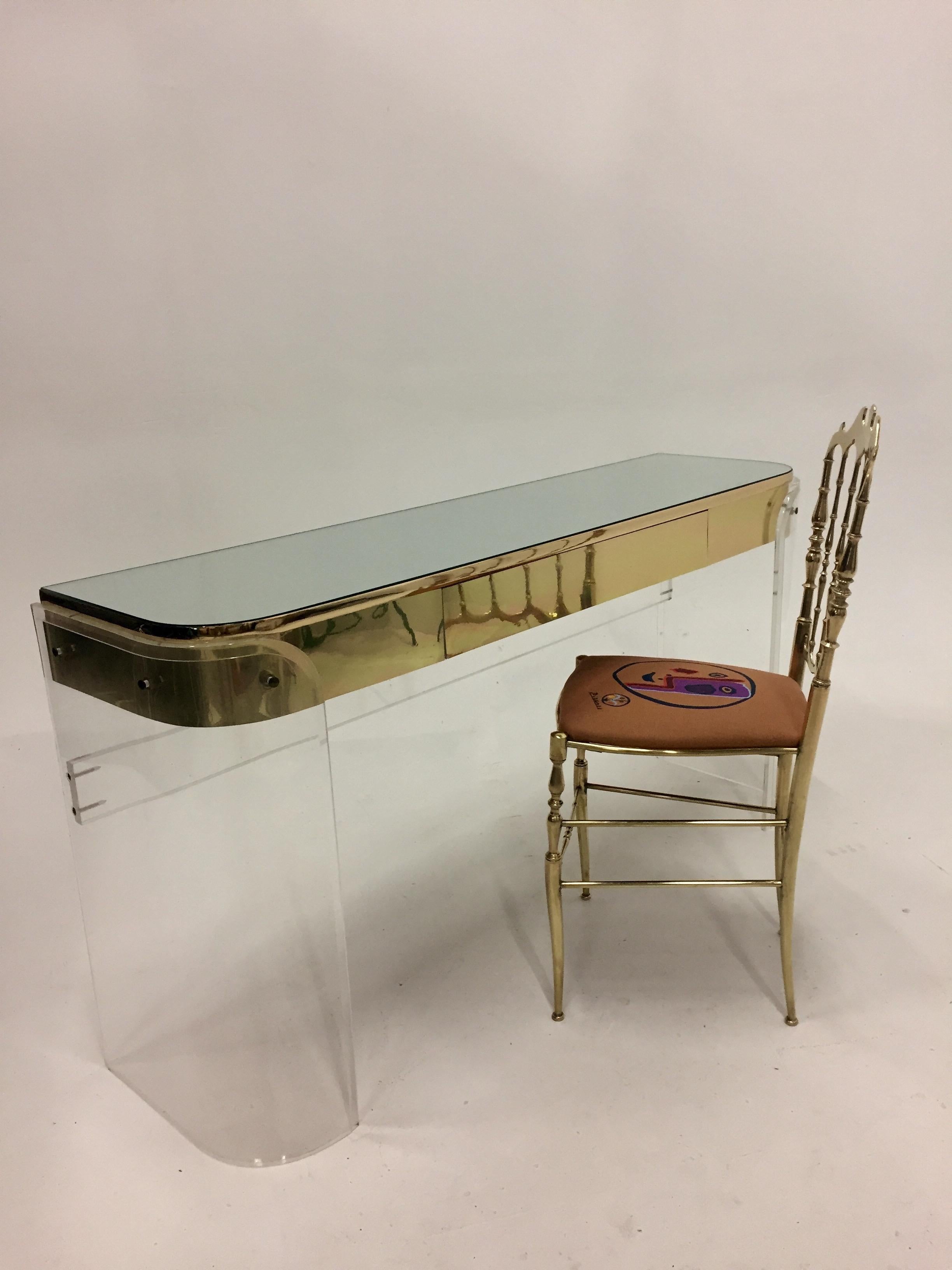 Glamorous Mid-Century Modern Lucite curved vanity or console having gold metal detailing, middle drawer, Lucite stretcher on the back and mirrored top.
The space from the floor to the base of the drawer is 24 inches.