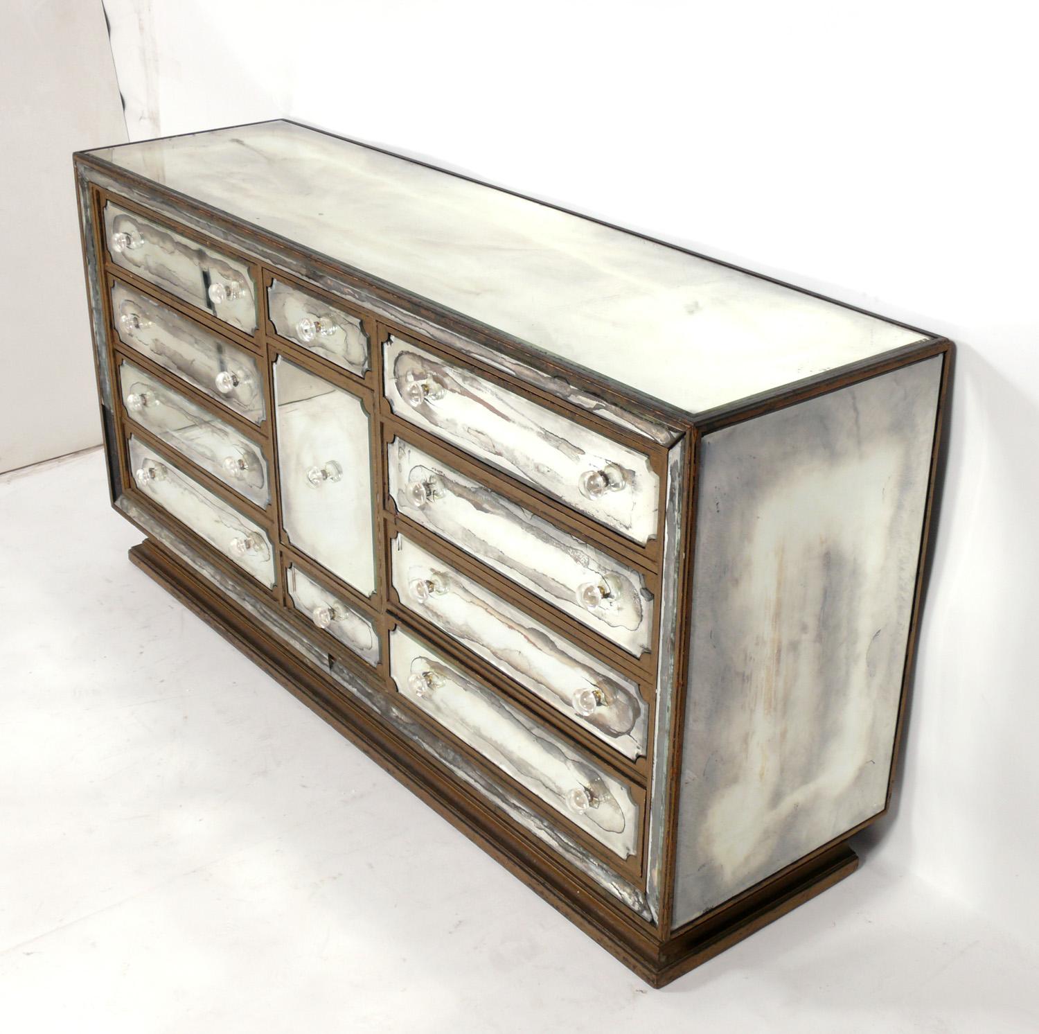 Glamorous mirrored chest, American, circa 1940s. Retains it's wonderful distressed original patina. It offers a voluminous amount of storage with 8 deep, wide drawers and two smaller central drawers and a center door that opens to reveal a