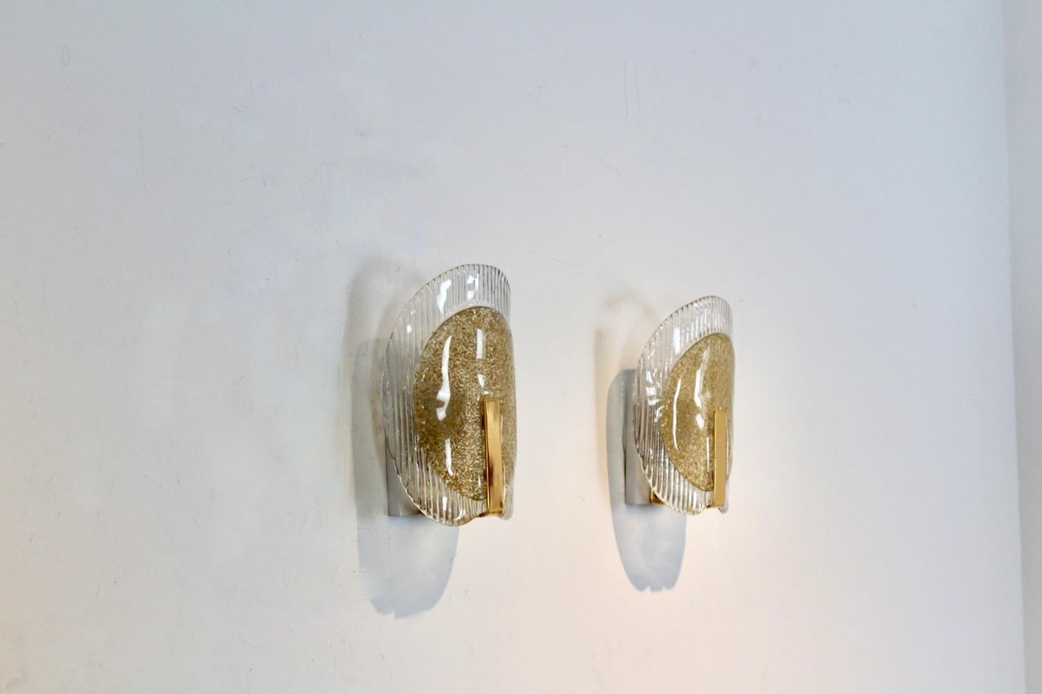 Highly sophisticated pair of Brass and Murano Glass Sconces produced in Italy Milano, ‘80’s. Each lamp has a handsome Brass plate and a beautiful full Murano Glass piece with gold flakes in the middle. The beautiful Murano glass fits perfectly in