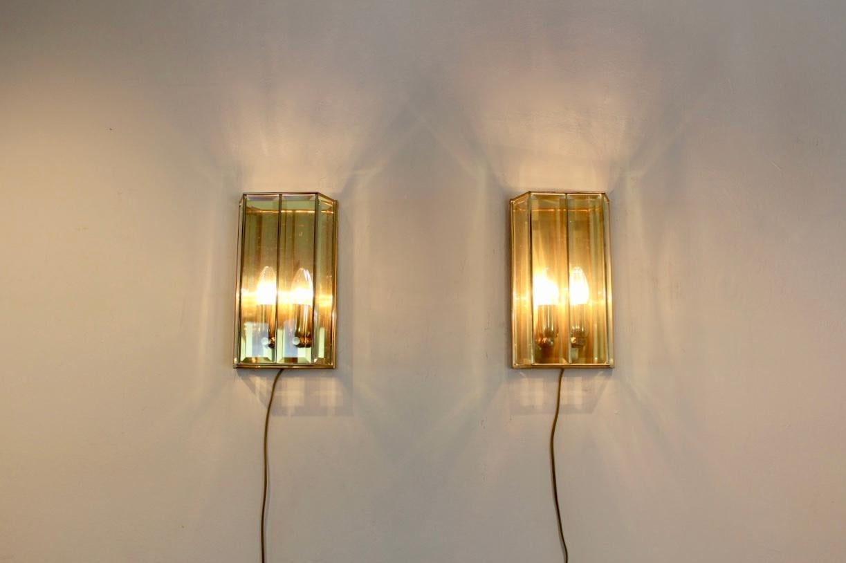 Highly sophisticated pair of brass and facet glass sconces produced in France, 1980s. Each lamp has a handsome brass back plate and frame and has a beautiful geometrical pattern with 4 full glass facet glass pieces. The beautiful glass fits