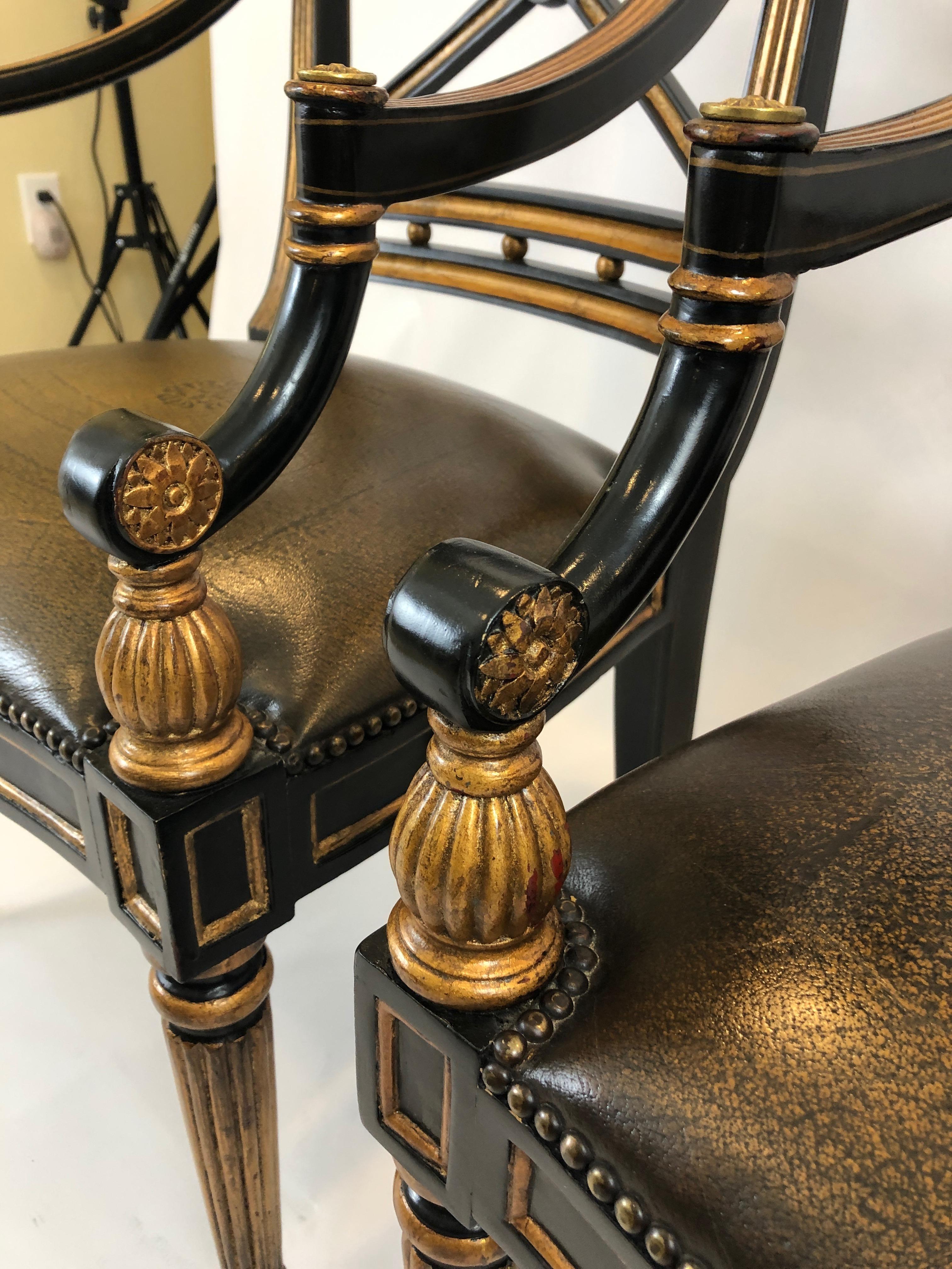 Glamorous pair of Regency style black and gold armchairs having wonderful X-style backs, gilded decorations including center rosettes and carved balls at the arms. Sumptuous embossed leather seats add to the luxury of these impressive