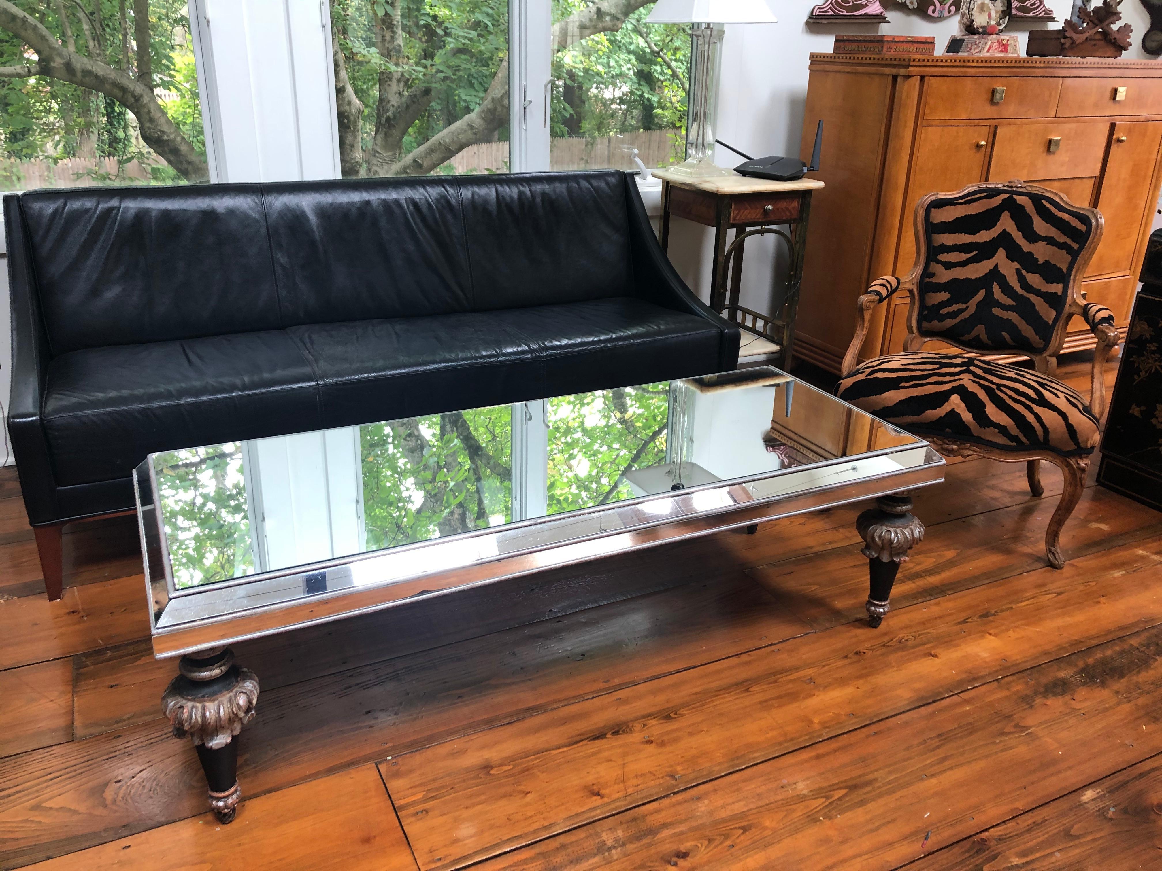 A sleek long and glamorous coffeetable having elaborately carved decorative legs painted black and silver with some of the original reddish underpaint showing through in places. The reflective mirrored top and sides were added later.