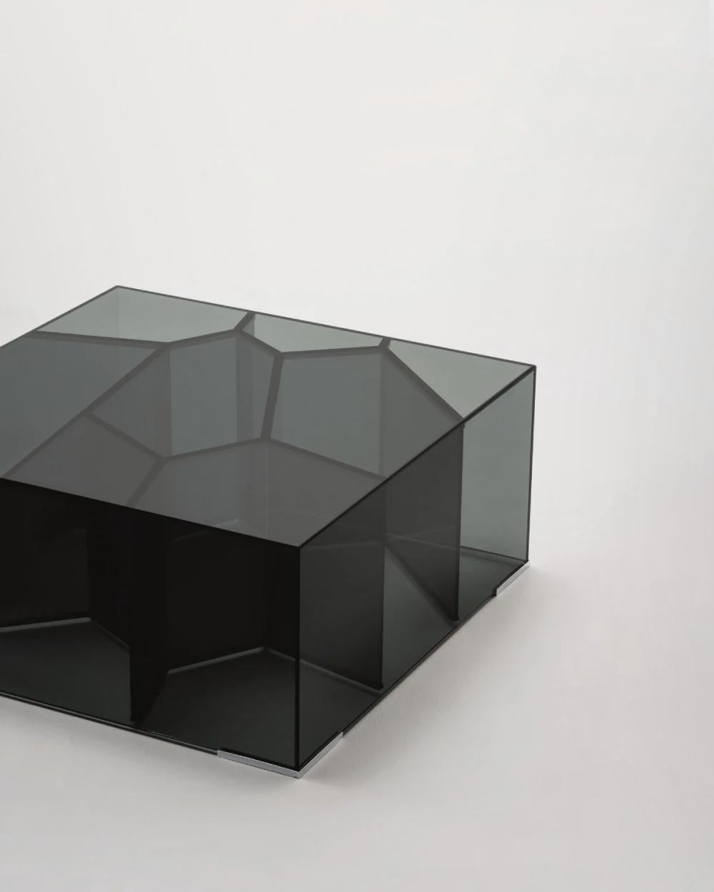 Serie von parallelepipedischen niedrigen Tischen aus 6 mm gehärtetem Rauchglas, 45° geklebt, dessen Innenseite eine komplexe Wabenstruktur enthält. Vier kleine verchromte Füße heben das Volumen leicht vom Boden ab. Erhältlich in zwei verschiedenen