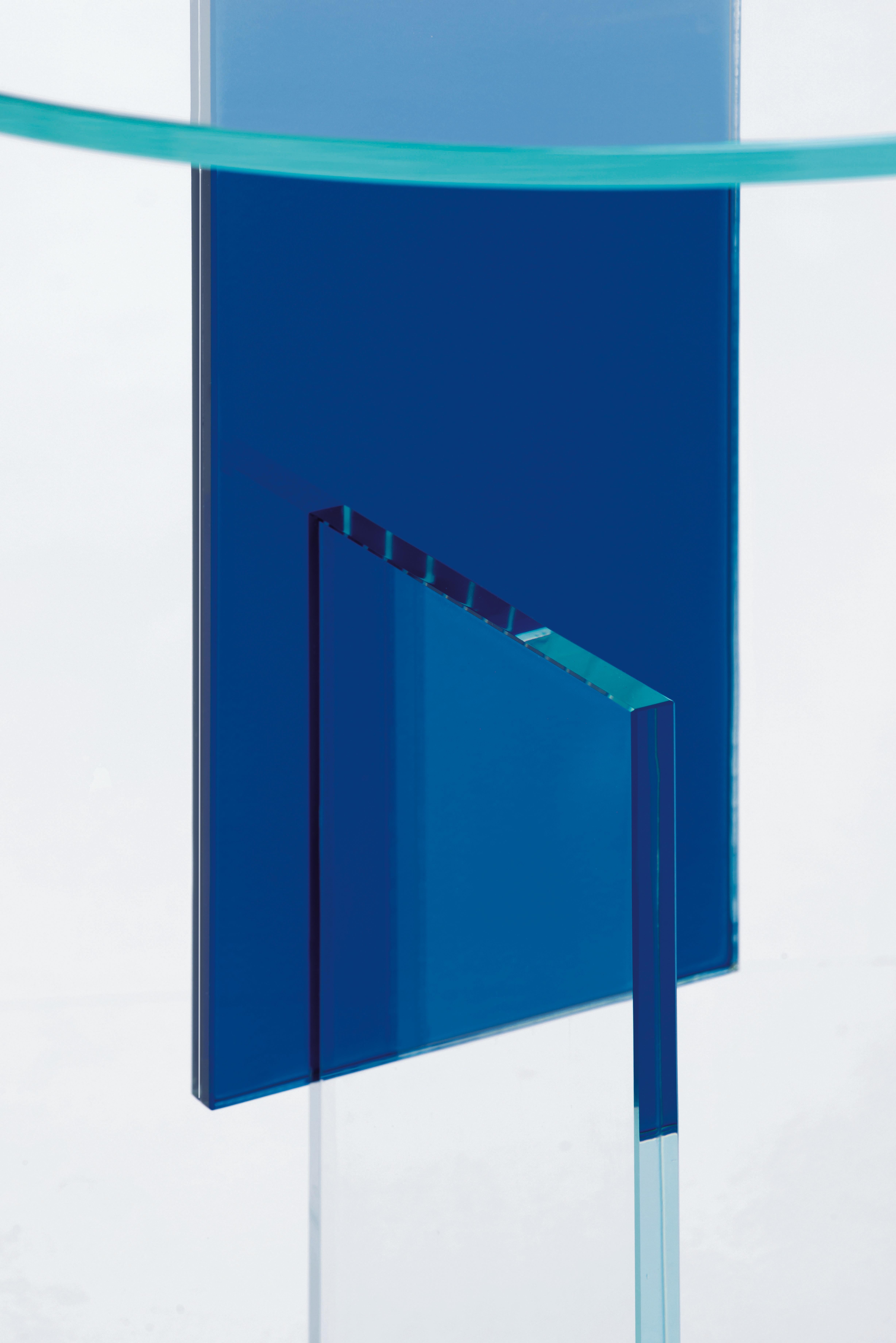 Niedriger Tisch mit Sockel, der durch das Zusammenkleben mehrerer gehärteter Glasplatten entsteht. Es gibt eine Version komplett aus Rauchglas und eine Version aus transparentem extraleichtem Glas mit einem Einsatz aus transparentem blauem, gelbem