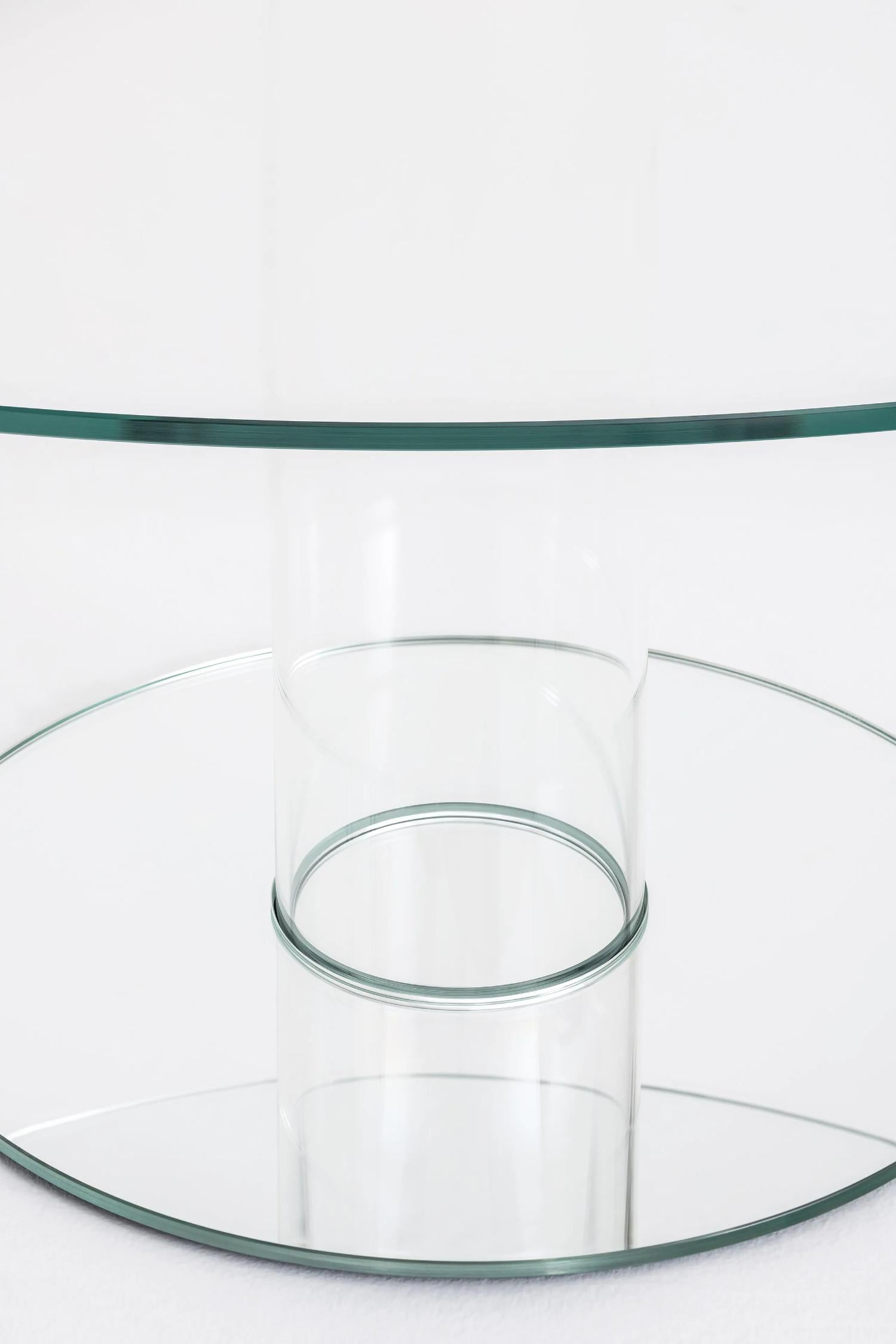 Serie di tavoli alti rotondi. Il piano in vetro temperato di 12 mm di spessore è sostenuto da una base composta da un cilindro cavo in vetro borosilicato e da un piede in vetro di 12 mm di spessore che funge da zavorra. Il piano e il piede sono