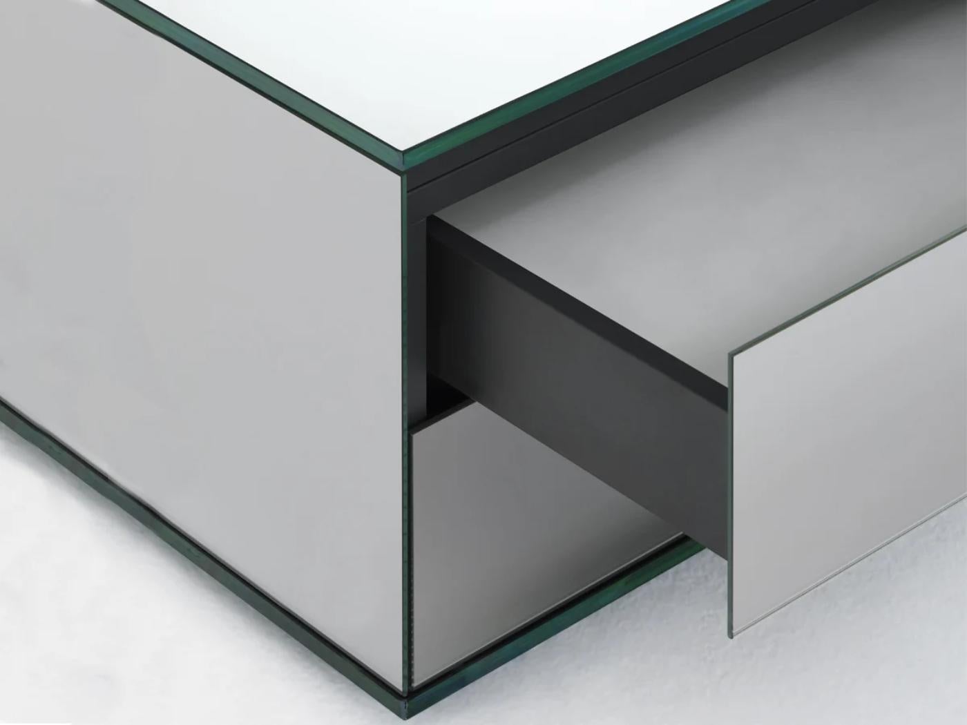 Low table with top and base in extra clear tempered 12 mm glass. The cantilevered top is supported by a drawer unit with push-pull blumotion opening drawers, covered with mirror joined at 45°. The base is completely mirrored, whilst the top is