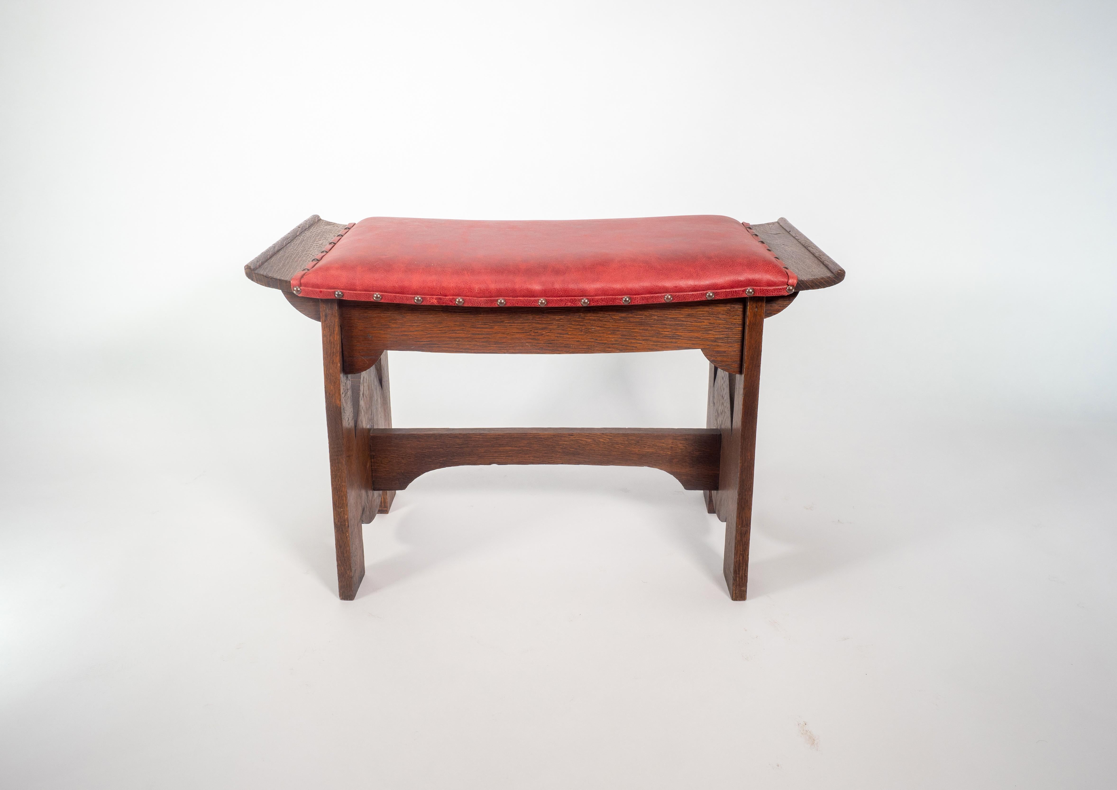 Glasgow School. George Logan attributed. An Arts and Crafts oak stool with upturned sides with quarter circle supports below and teardrop cut-outs to the sides, united by a shaped stretcher. Professionally re-upholstered in a red leather.