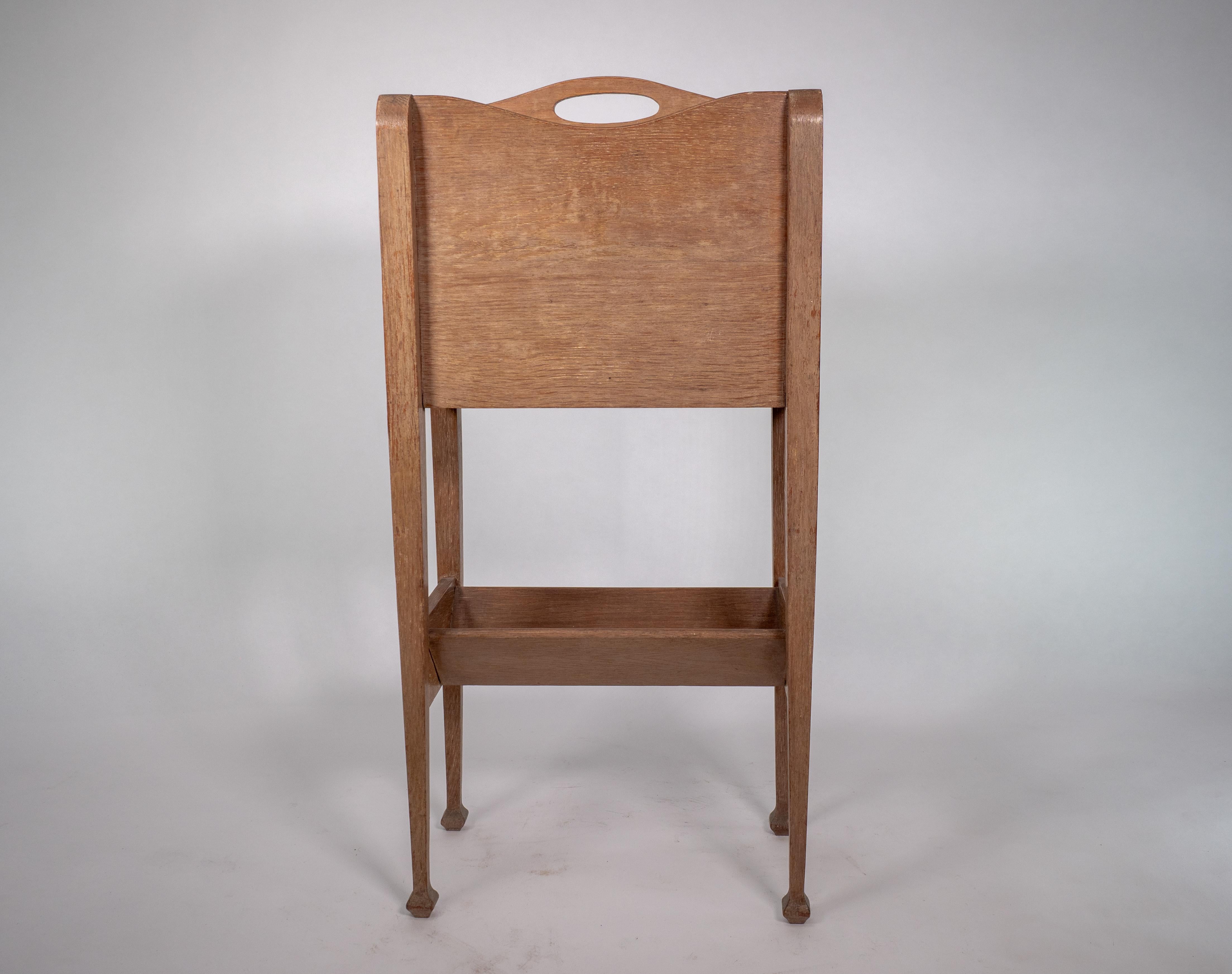 Glasgow School. Style of George Walton. An Arts and Crafts oak magazine and book rack with pierced oval carry handle to the top and opposing shaped upper sides with a book trough to the base uniting the square tapering legs.
