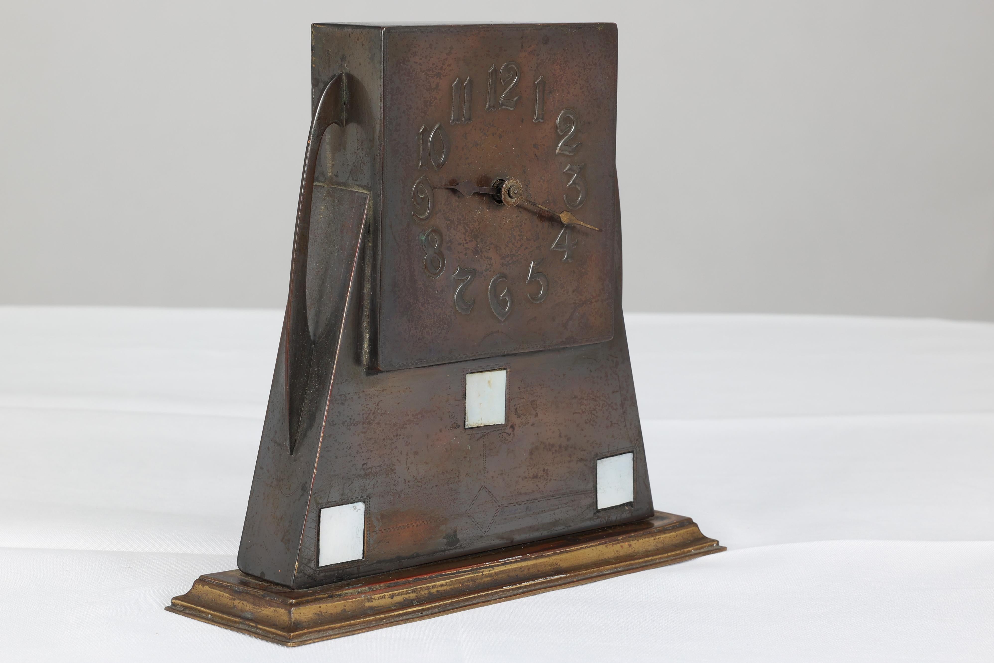 Reloj de latón patinado de la Escuela de Glasgow de Artes y Oficios, con detalles cuadrados de incrustaciones de nácar y asas de latigazo en los laterales.