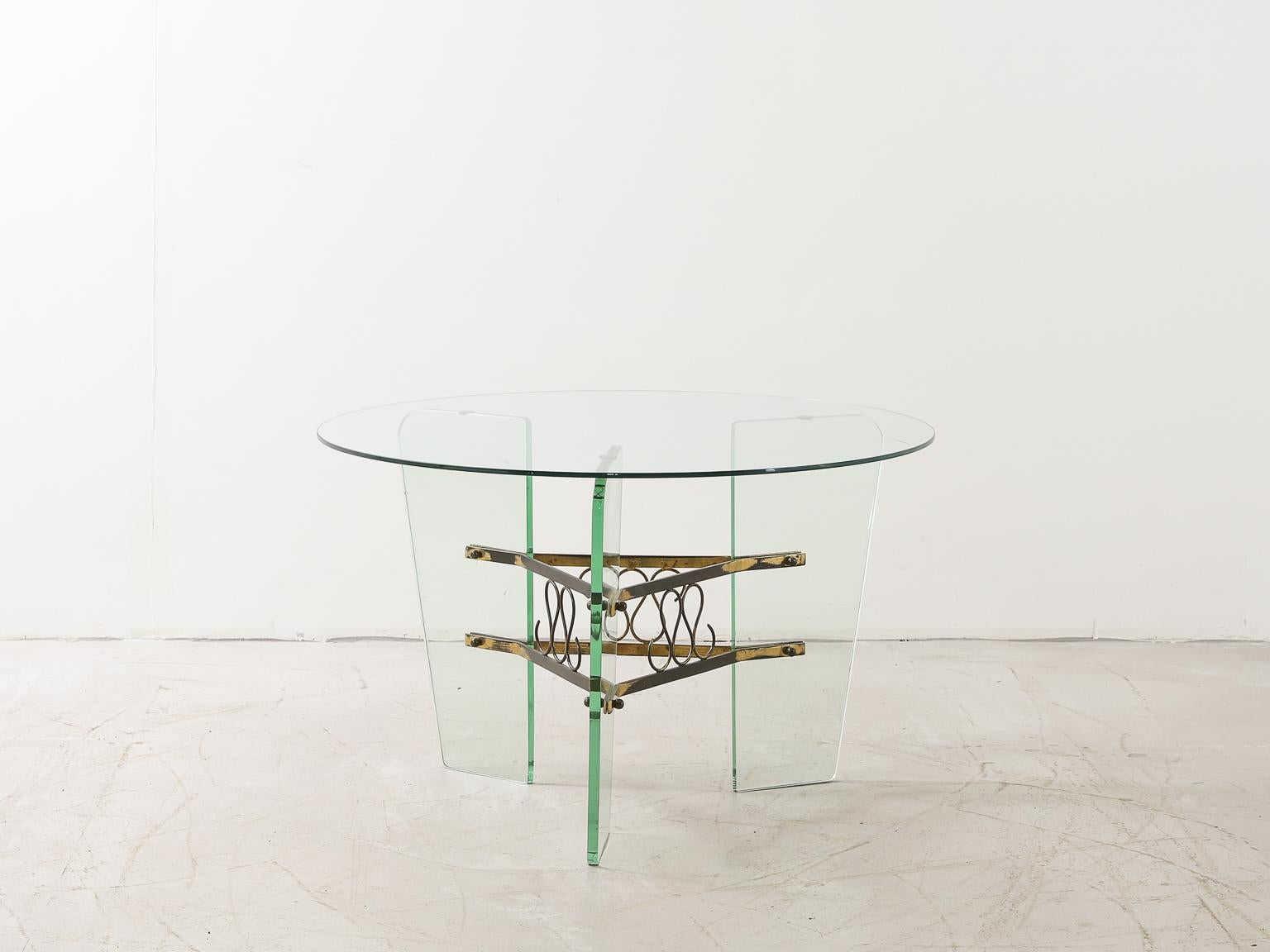 An elegant glass and brass coffee or smoking table by Italian designer Luigi Brusotti, from the 1950s.

With a circular glass top held by three glass legs connected by an ornate, decorative brass element.