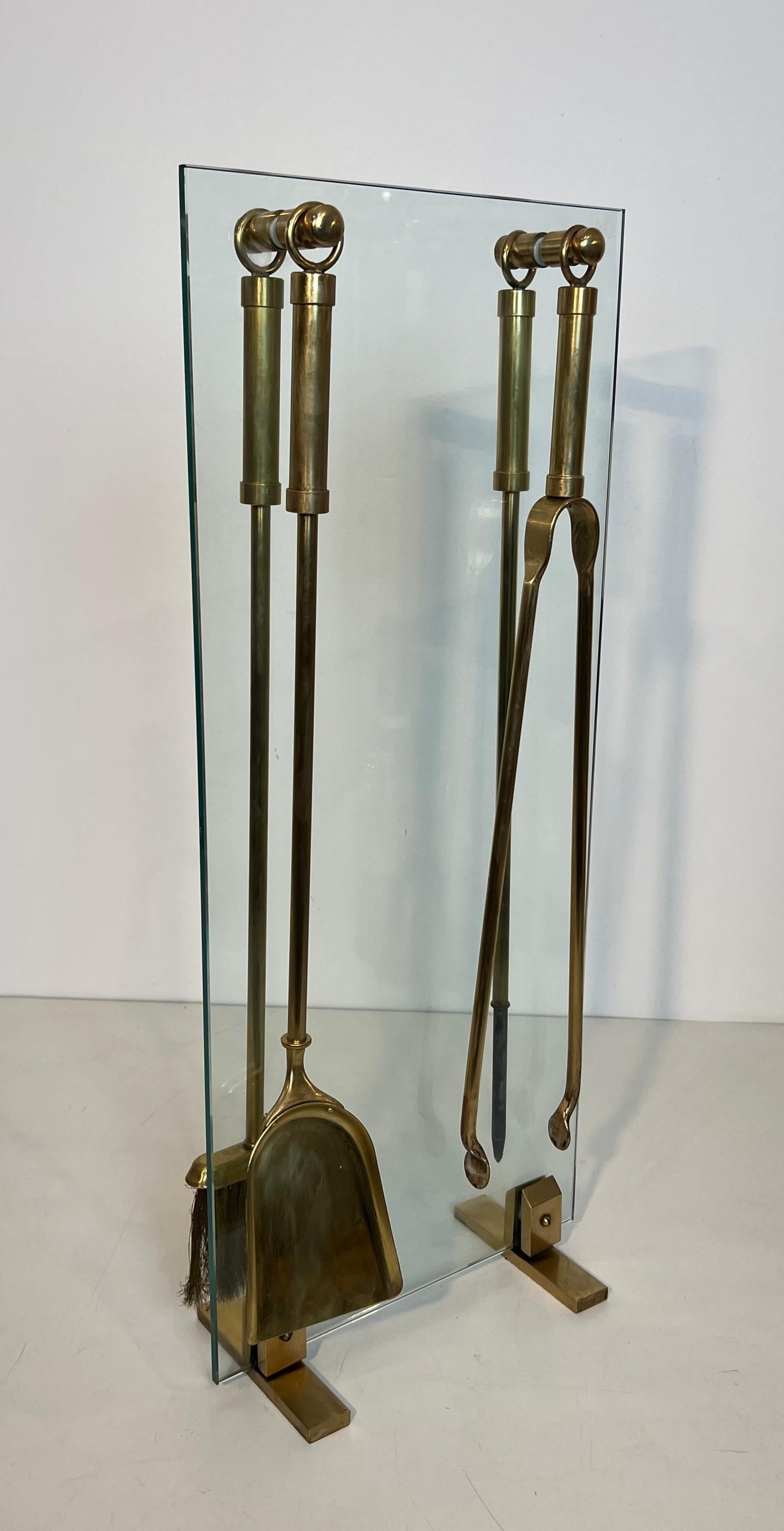 Esta chimenea de diseño bonito y elegante está hecha de cristal con elementos y herramientas de latón. Se trata de una obra francesa. Alrededor de 1970