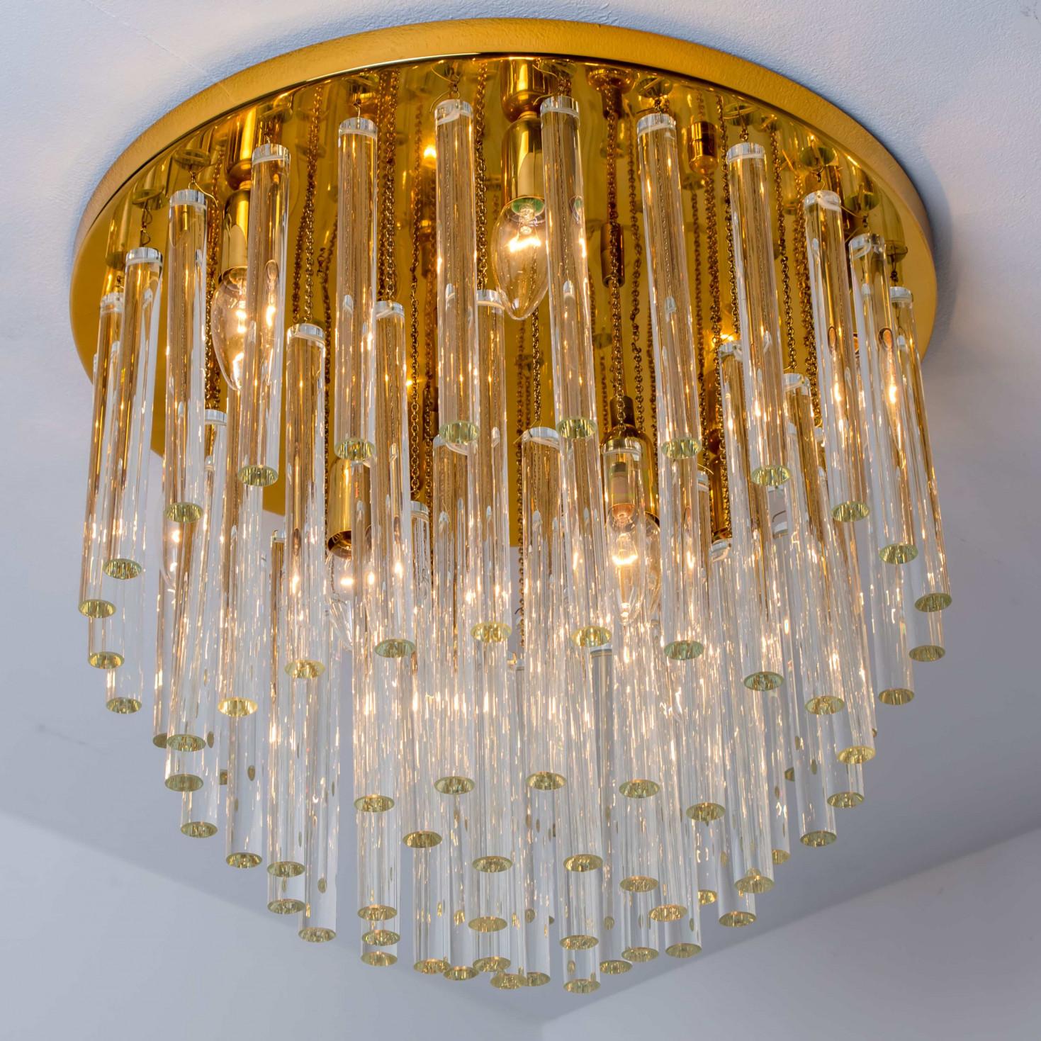 This high quality chandelier by Palme (1970) features a round, polished brass ceiling plate from which numerous clear glass tubes are suspended in varying lengths. The glass elements are individually attached to the base with small brass