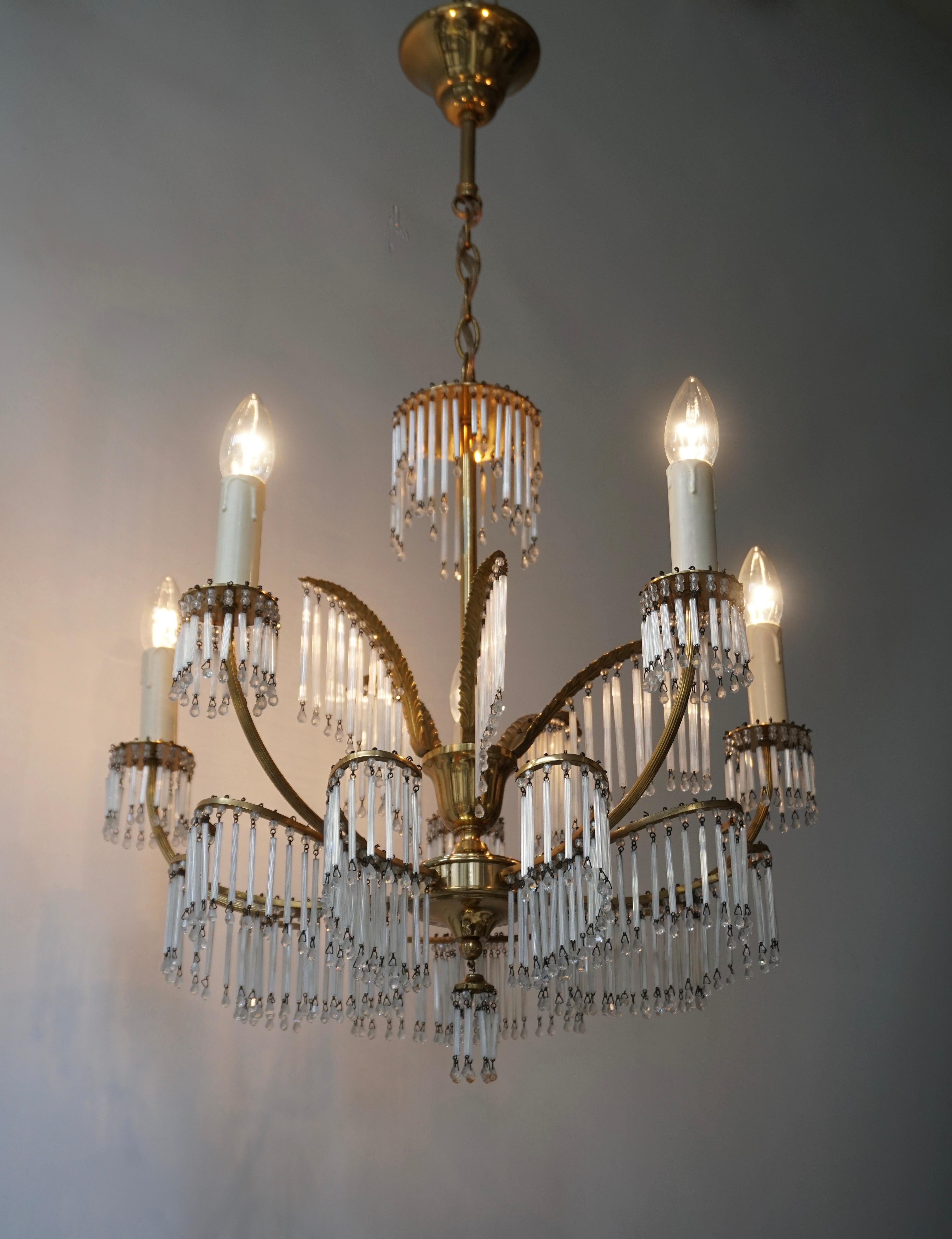 Superb gilt brass chandelier with issuing elegant leaves from which hang glass rods. Glamorous Maison Jansen style brass palm frond chandelier with glass tubes, circa 1950s. Retains warm original patina.
Maison Jansen was a Paris based interior