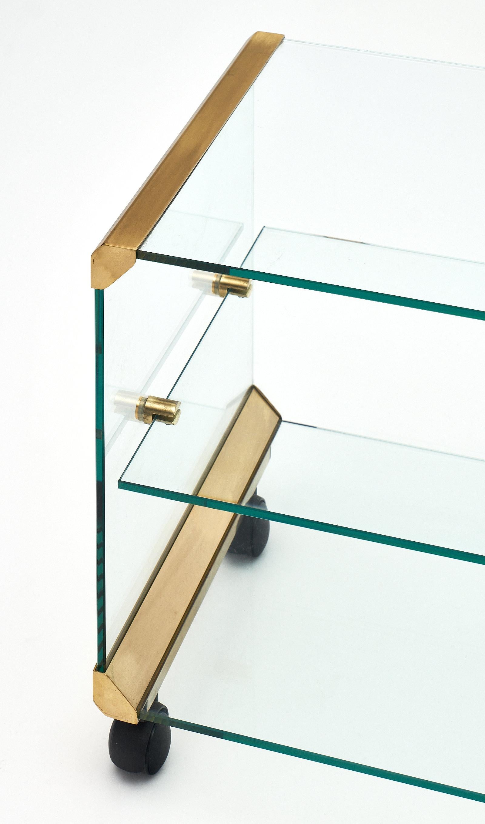 Italian modernist glass and brass side table with one glass shelf and supported by casters. The glass structure is held together with the original brass hardware and corners. We love the unique style and quality of this piece.