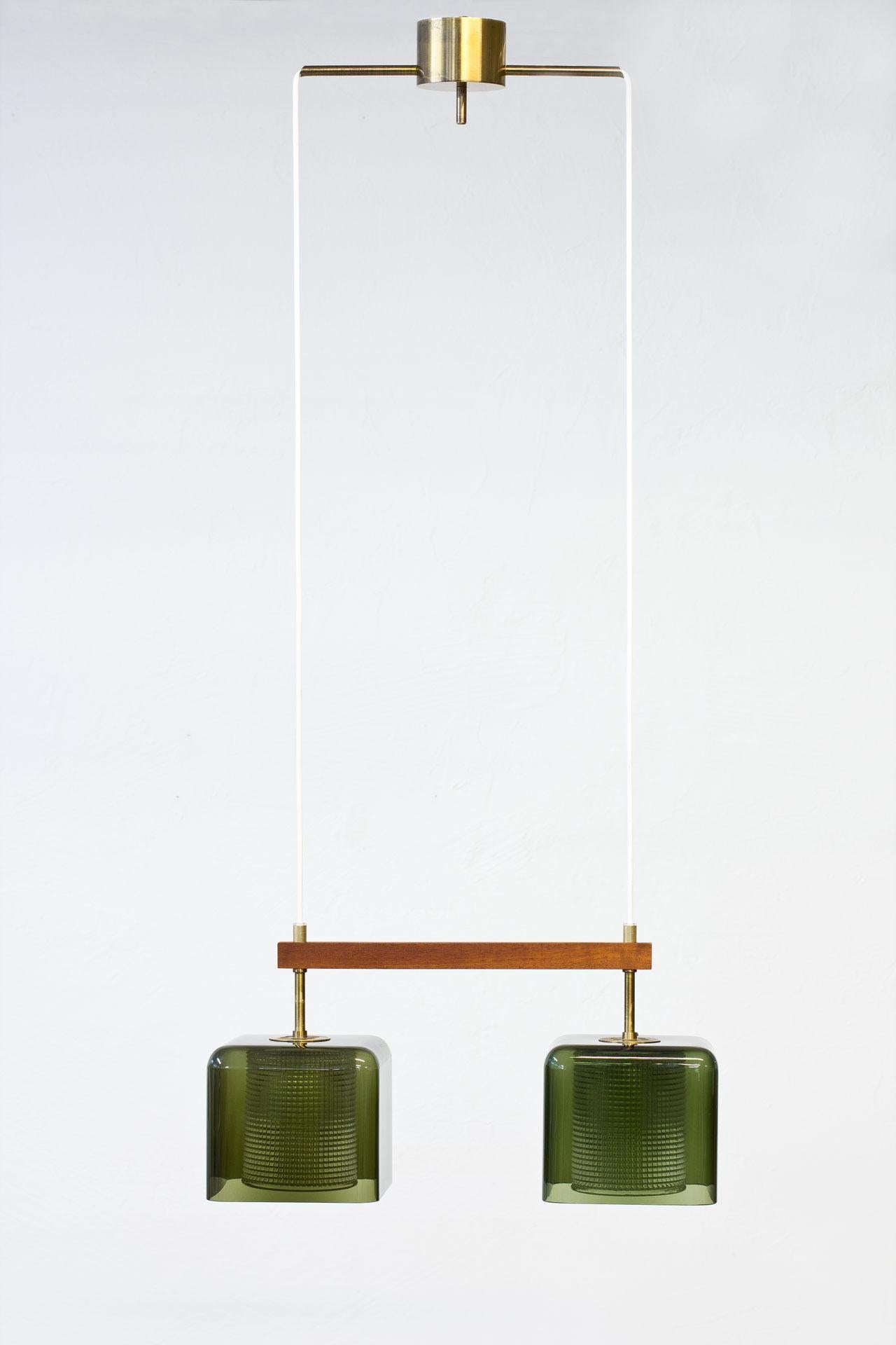 Pendant lamp designed by Carl Fagerlund for Swedish glass company Orrefors. 
Manufactured during the 1960s. 
Square shaped cups in green tinted glass with internal clear pressed glass diffuser, framed by a teak stretcher. Brass fittings with