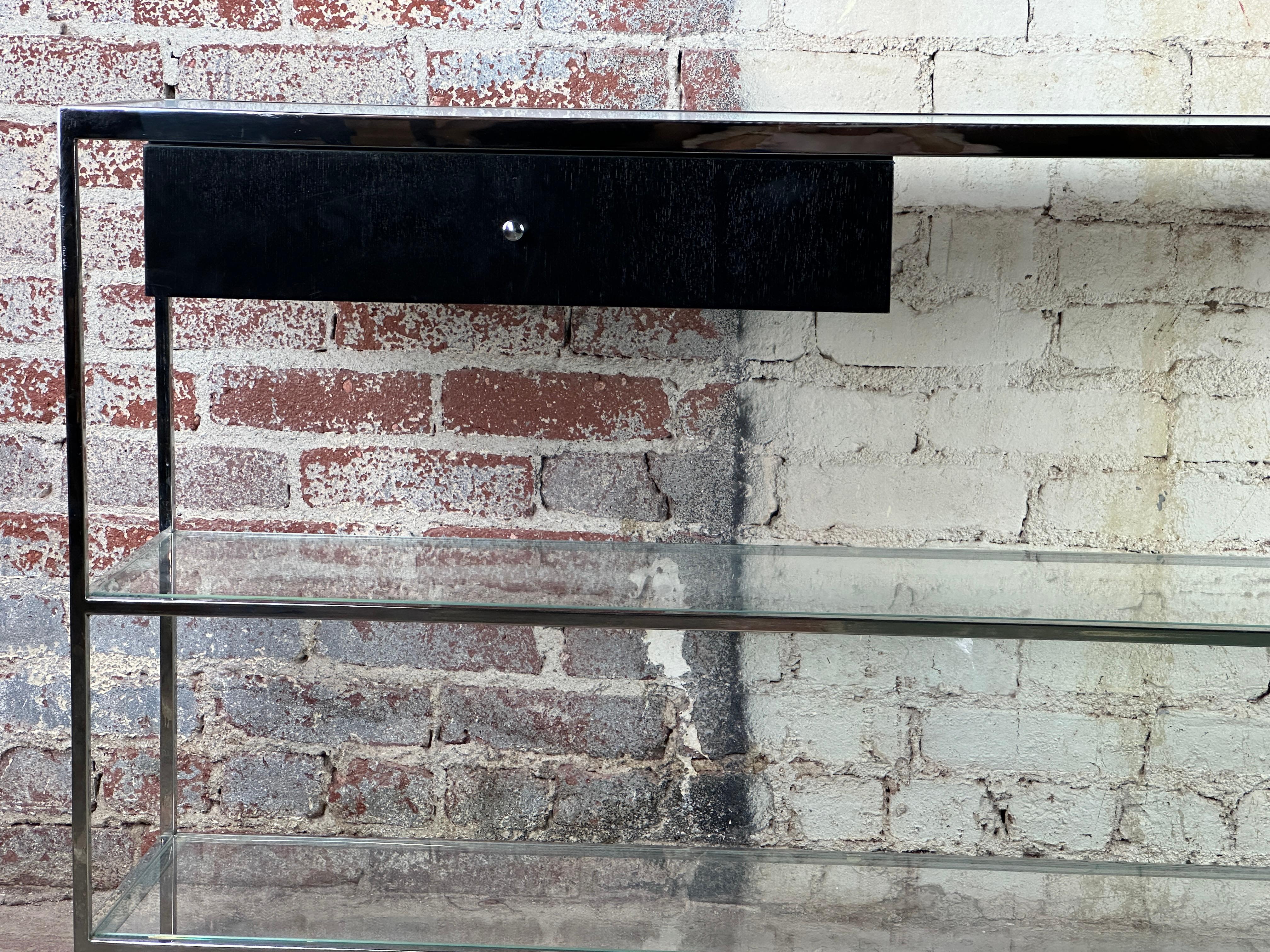 This console, inspired by the designs of Milo Baughman, features a sleek aesthetic that blends modern materials and classic style. The console's top is crafted from treated glass opaline, and the bottom shelves are made of clear glass.

On the left