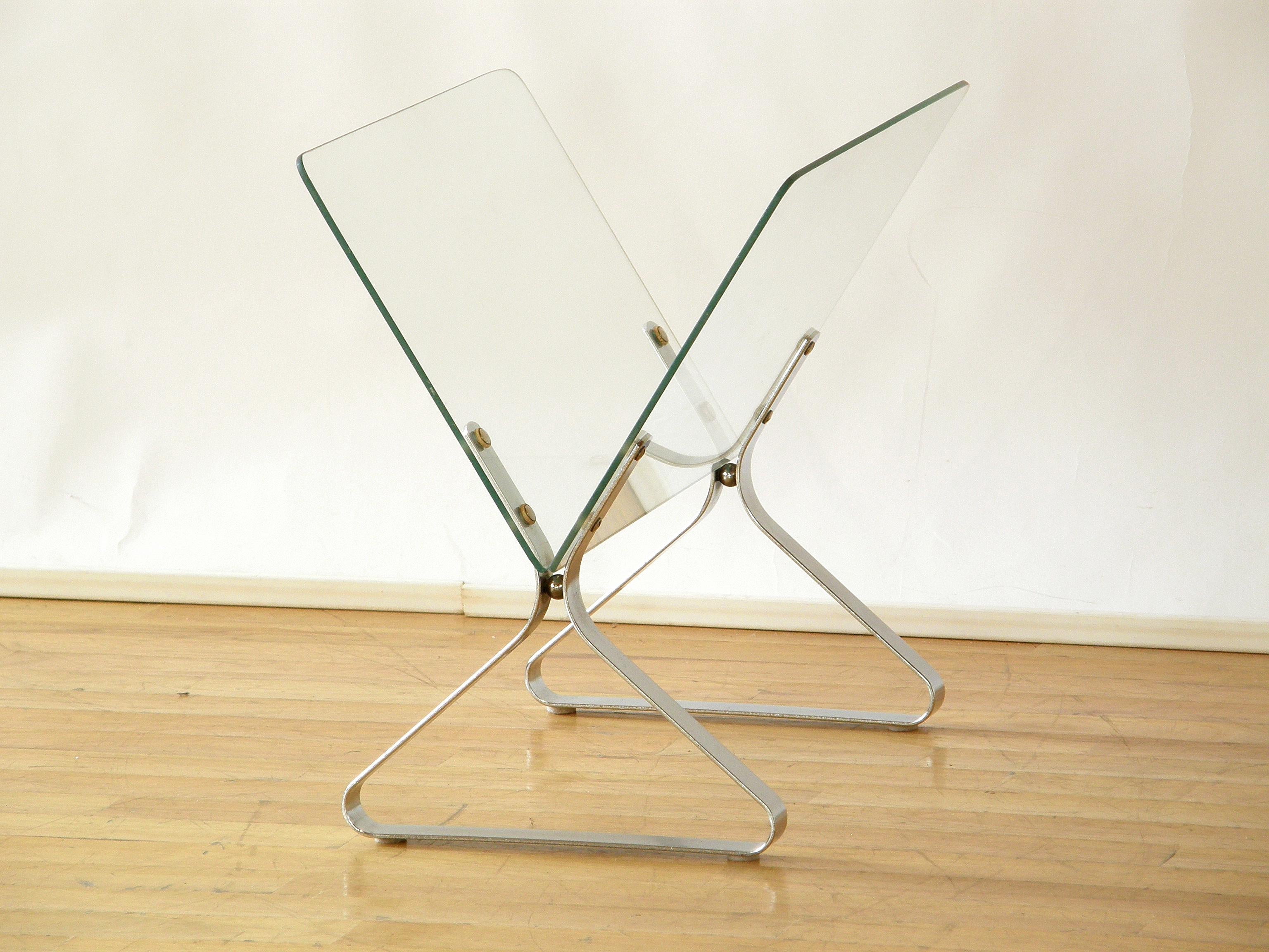 This circa 1970s, Minimalist magazine rack has glass plate sides and bent, chrome plated metal base pieces. The 