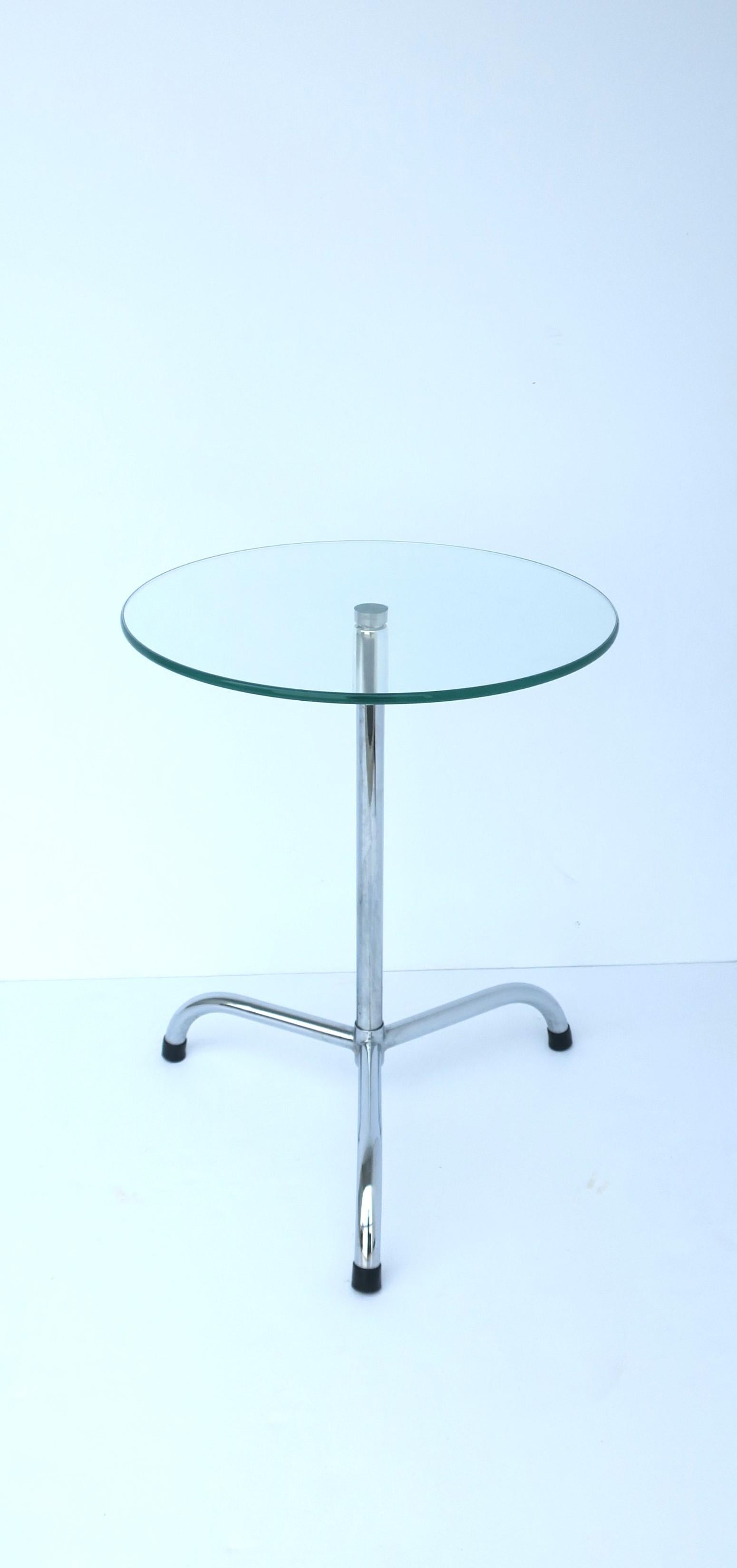 A chrome and glass side drink table in the Modern style, circa late-20th century, 1970s. Table has a round glass top with smooth flush surface and a chrome tri-pod base. A convenient table for dinks, cocktails, nuts, etc. Dimensions: 14.88