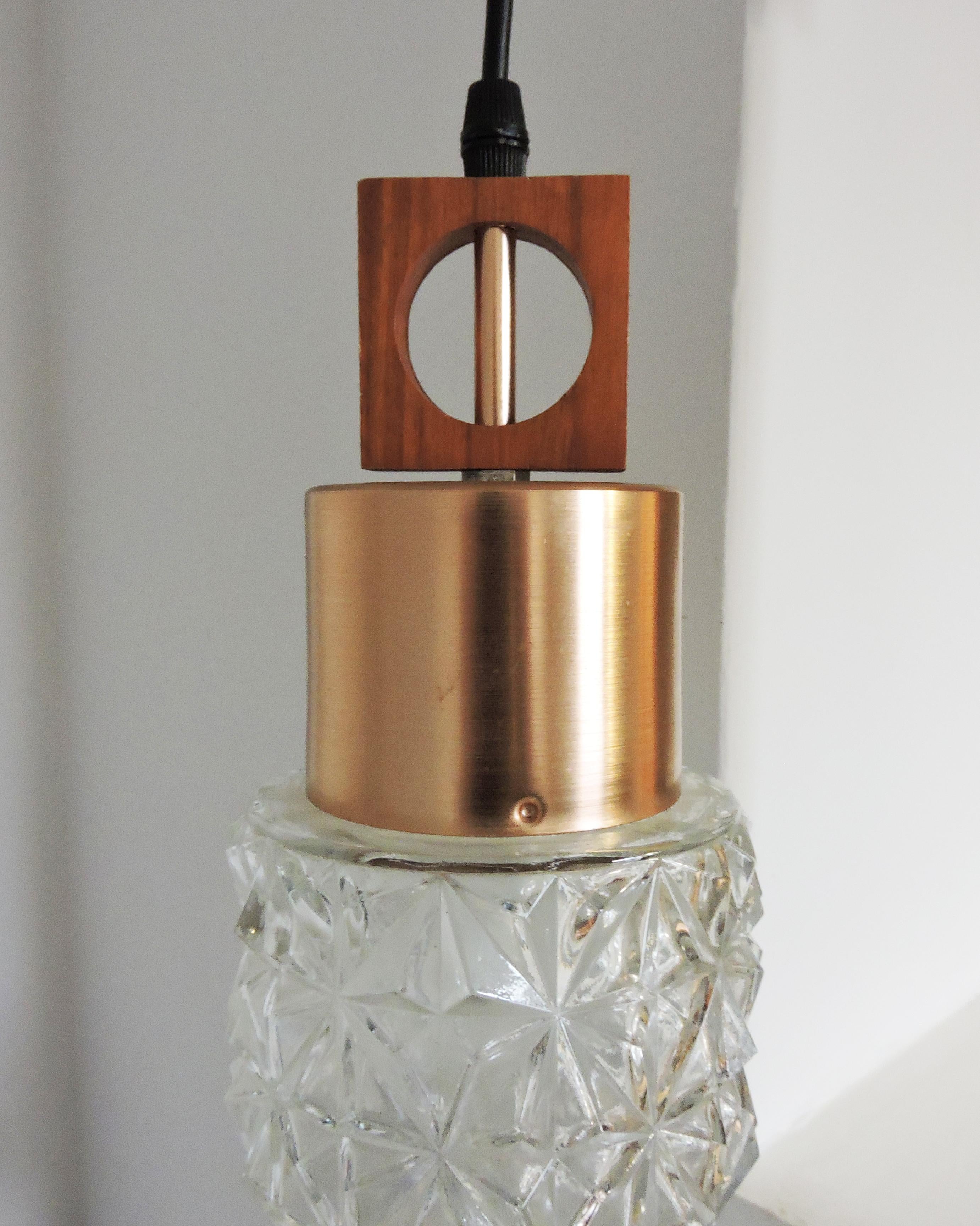 A 1970s glass and copper pendant light. The light hangs from a black wire and features a wooden square shape at the top.

A professional electrician has rewired this piece to be in working order.

Plug type - UK Plug (up to 250V).