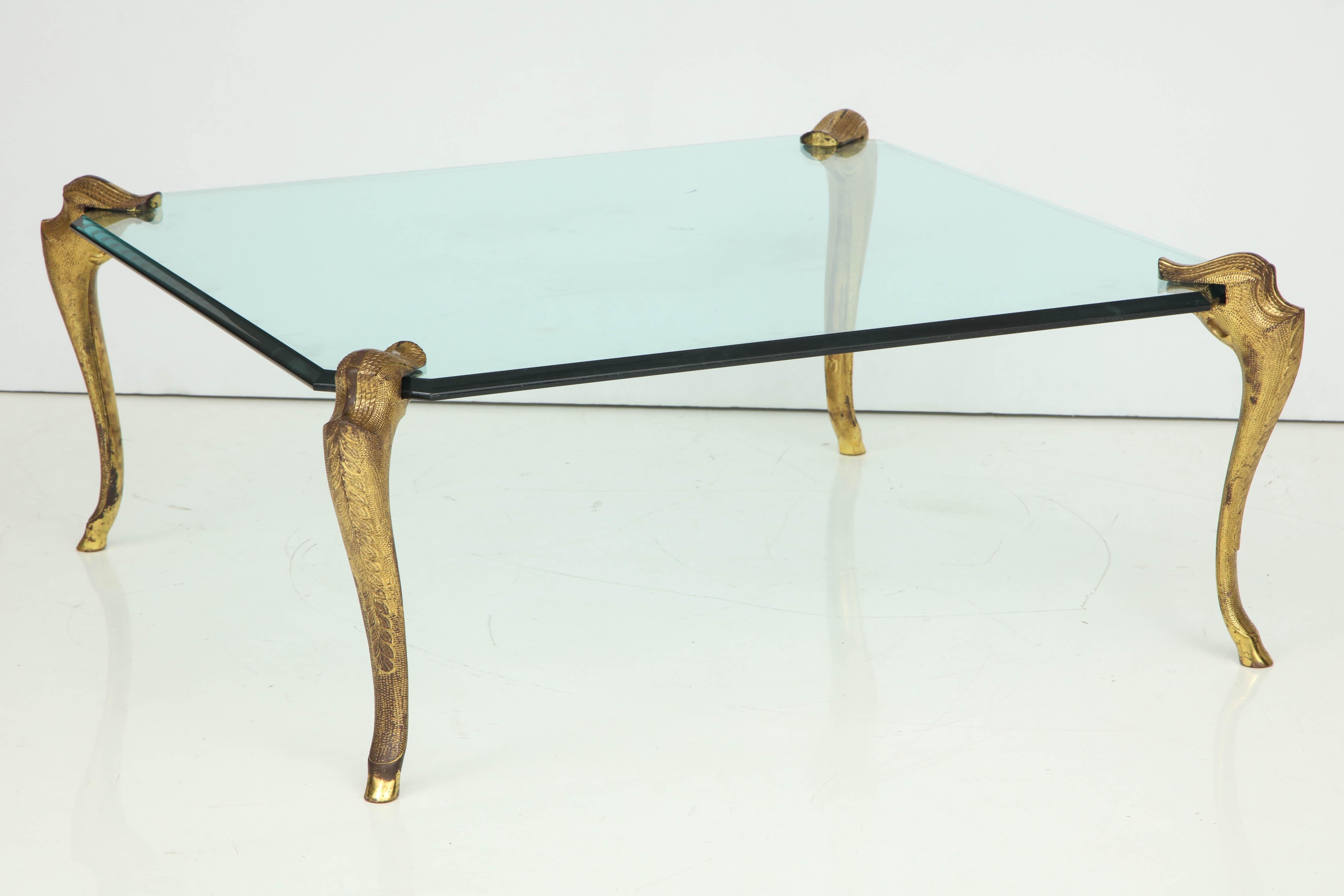 A stunning square cocktail table attributed to the decorative hardware firm, P.E. Guerin, The thick glass top is supported by four gilt bronze 