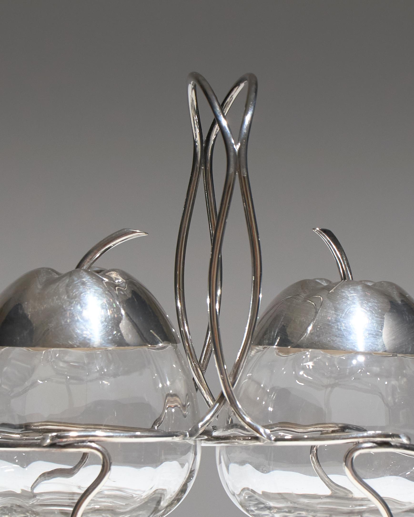Serviteur à confiture en verre et métal argenté, en forme de pomme ou de poire, années 1970. Il repose sur un support métallique aux formes ondulantes, évoquant des tiges végétales. Très bon état.