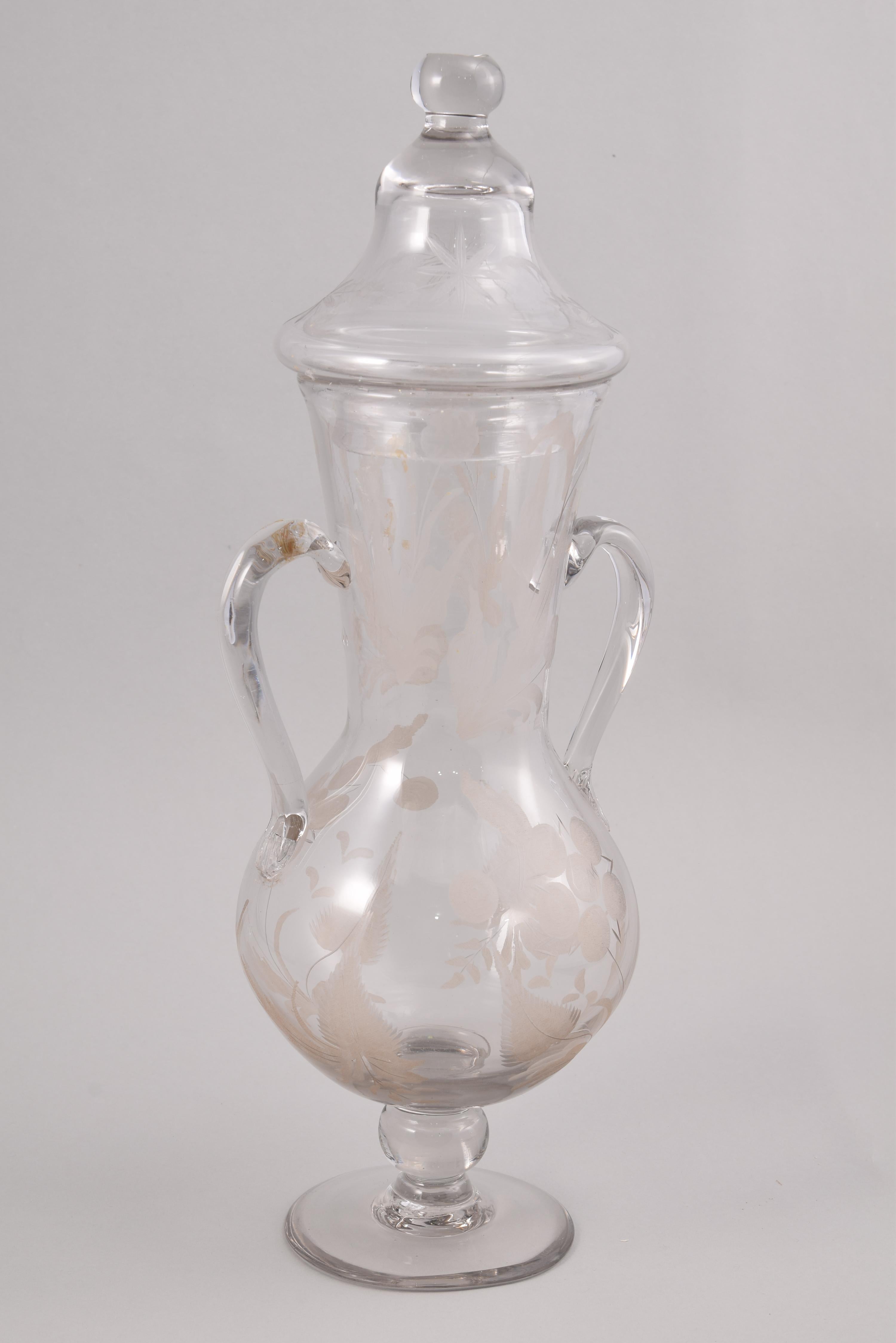 Jug and glass. Glass. Royal Glass Factory of La Granja de San Ildefonso, Segovia, Spain, 18th century. 
Pitcher or vase with lid and glass with a small spout made of cut and engraved transparent glass, decorated with plant elements and