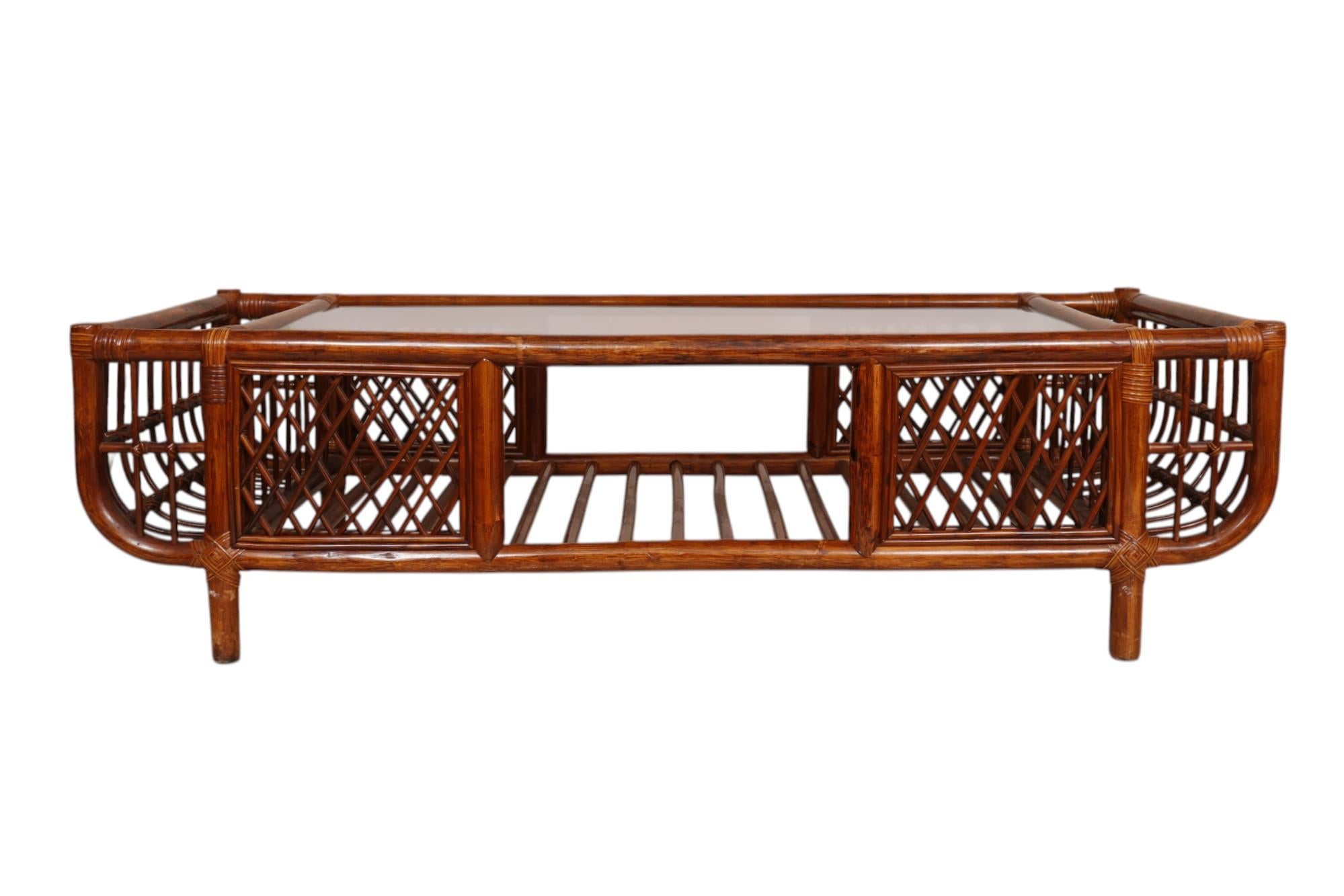 Table basse en bambou à plateau en verre, de style moderne, datant du milieu du siècle dernier. Teinté dans une riche couleur acajou, d'épaisses pièces de bambou forment le cadre avec des paniers à journaux/magazines en bambou en bois courbé aux