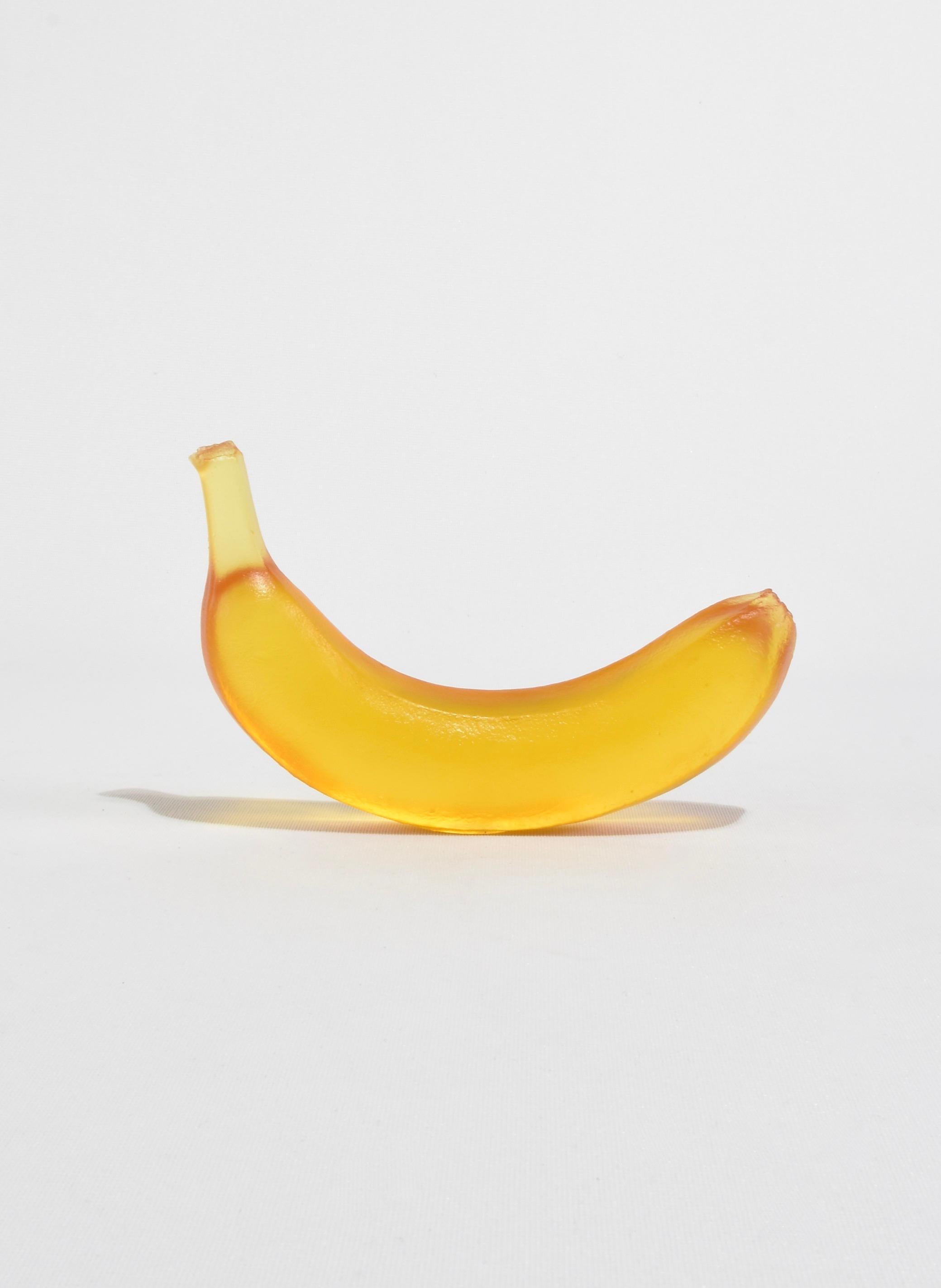 Casted glass banana in honey by Devon Made inspired by blown glass fruit makers and collectors from the 1960's. The light playful approach to everyday fruit is contrasted with the heaviness of the crystal glass, a unique material that catches and