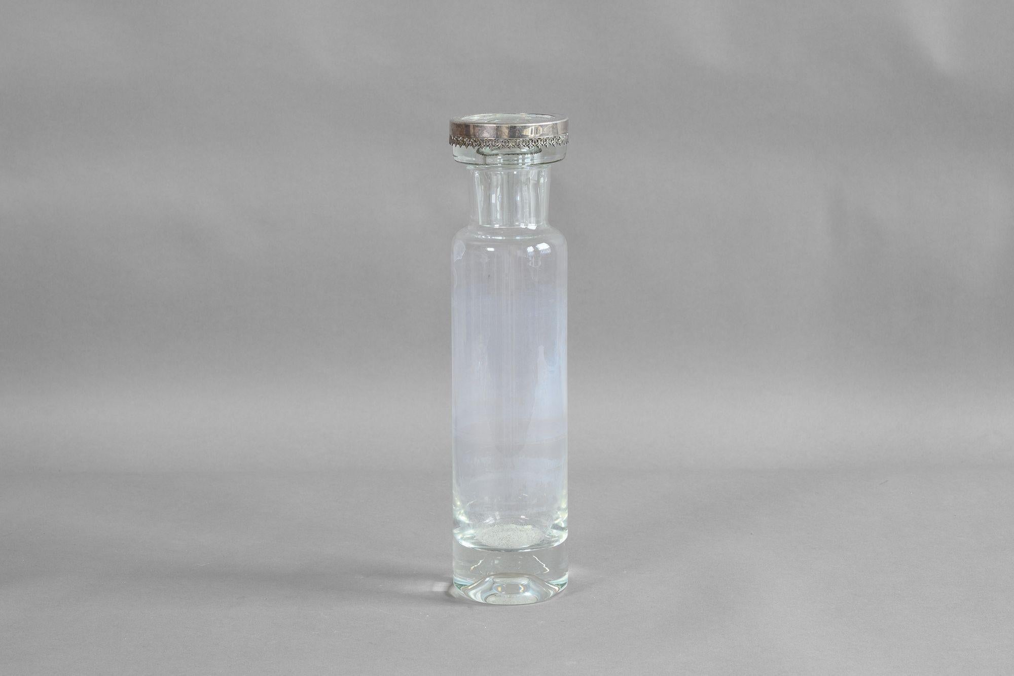 Grande bouteille en verre avec bord et bouchon en métal argenté.

K.K. vers 1930.

H 29cm x L 7cm x P 7cm