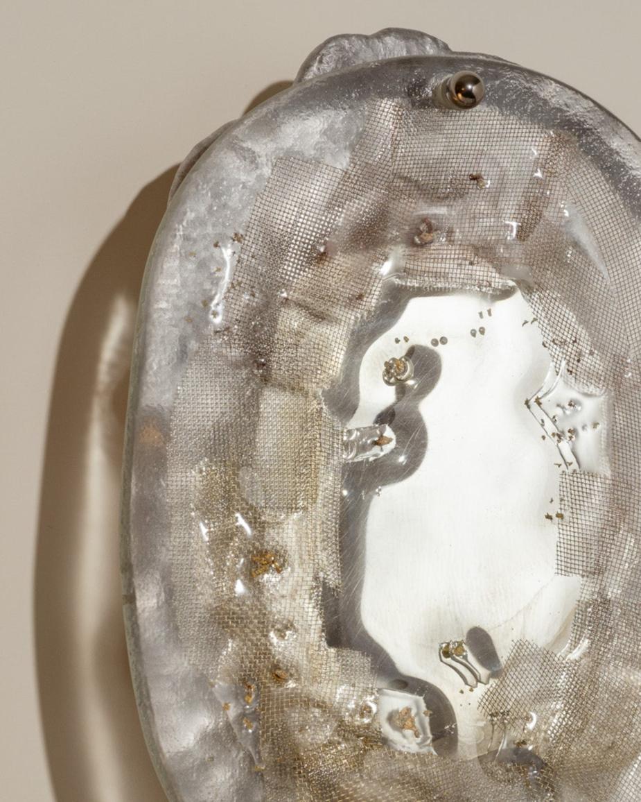 Applique murale en verre, laiton et aluminium (n°10). La struttura in laiton ospita una placca di vetro testurizzato, lavorata a mano in modo artigianale con inclusioni, bullette e un rivestimento in alluminio integrato nel materiale. Un miroir è