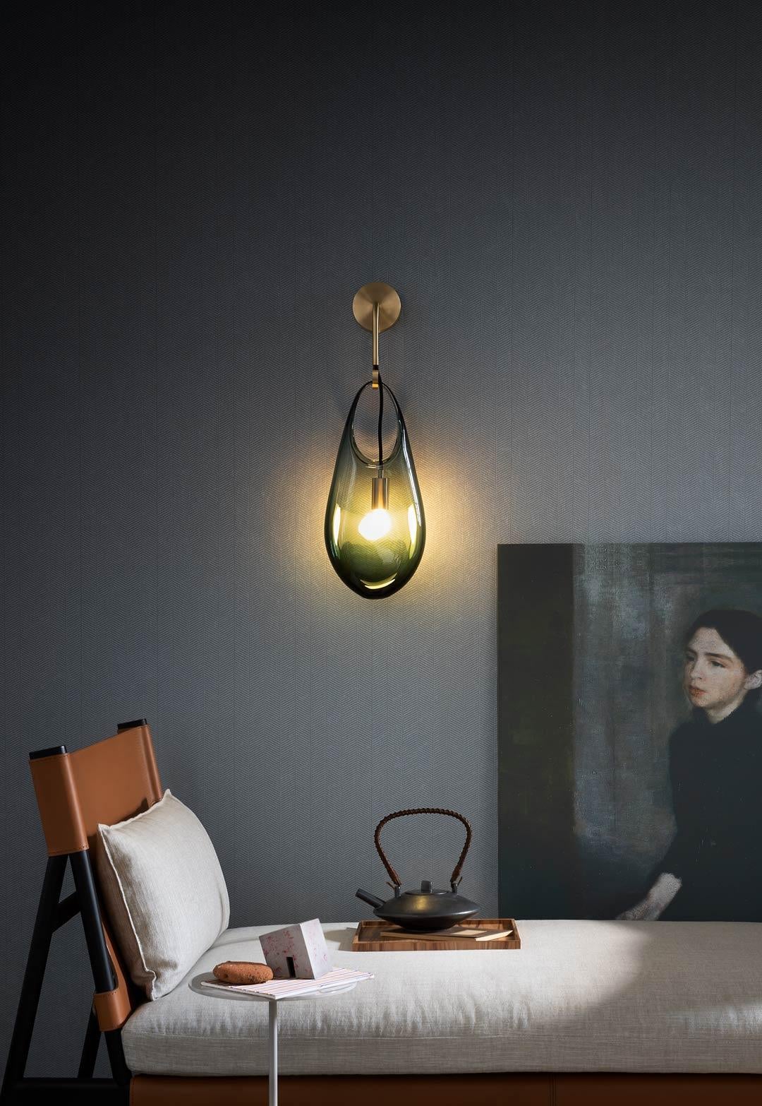 An expressive glass vessel that appears to droop from its hook as if molten serves as a shade on this wall sconce. Available in two sizes. The socket is suspended from the hook on a fabric-wrapped electrical cord and is loosely suspended within the