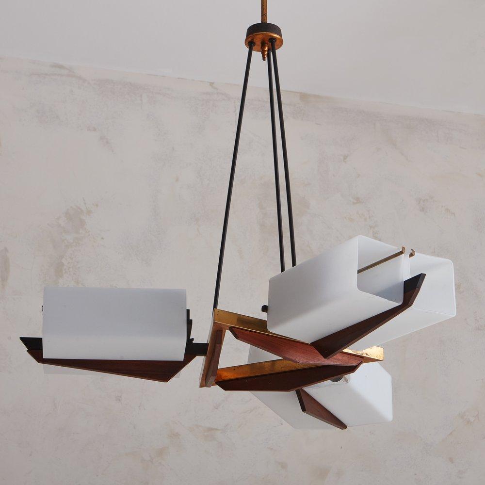 A midcentury Italian chandelier designed by Bruno Chiarini in the 1950s. This fixture has a triangular patinated brass frame with subtle carved wood detailing on the underside. Three angular wood arms extend from the sides and each arm supports two