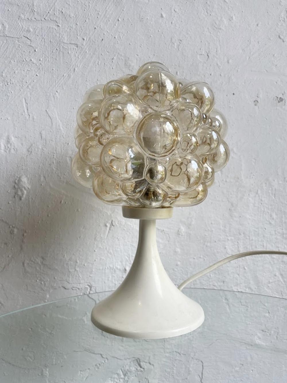 Esta característica lámpara de sobremesa de cristal burbuja fue diseñada por la finlandesa Helena Tynell para el fabricante alemán Glashütte Limburg a finales de la década de 1960 y principios de la de 1970. La lámpara presenta una característica