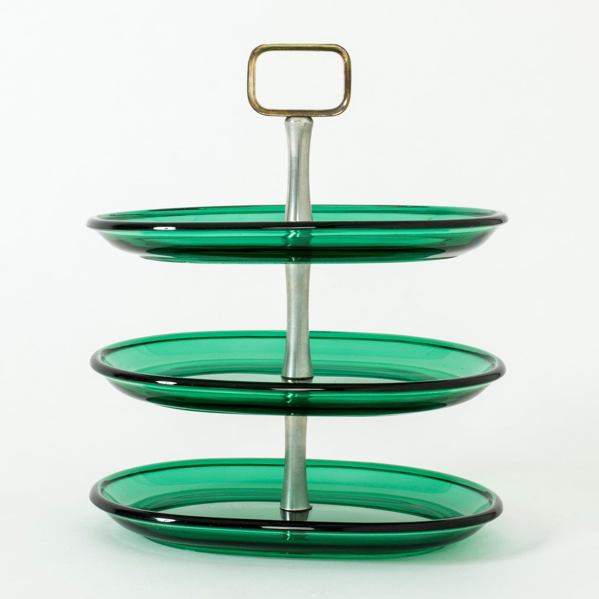 Beautiful cake stand with three stories by Josef Frank. Oval trays in thick, vibrant green glass. Handle made from steel with a large, brass handle. Clean lines and beautiful combination of materials.